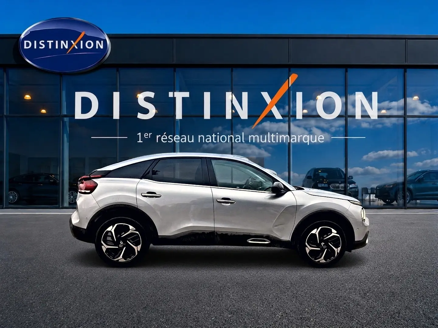 Profil droit d'une Citroën C4 gris métallisé 2024, avec jantes alliage et vitres arrière surteintées, devant une vitrine Distinxion.