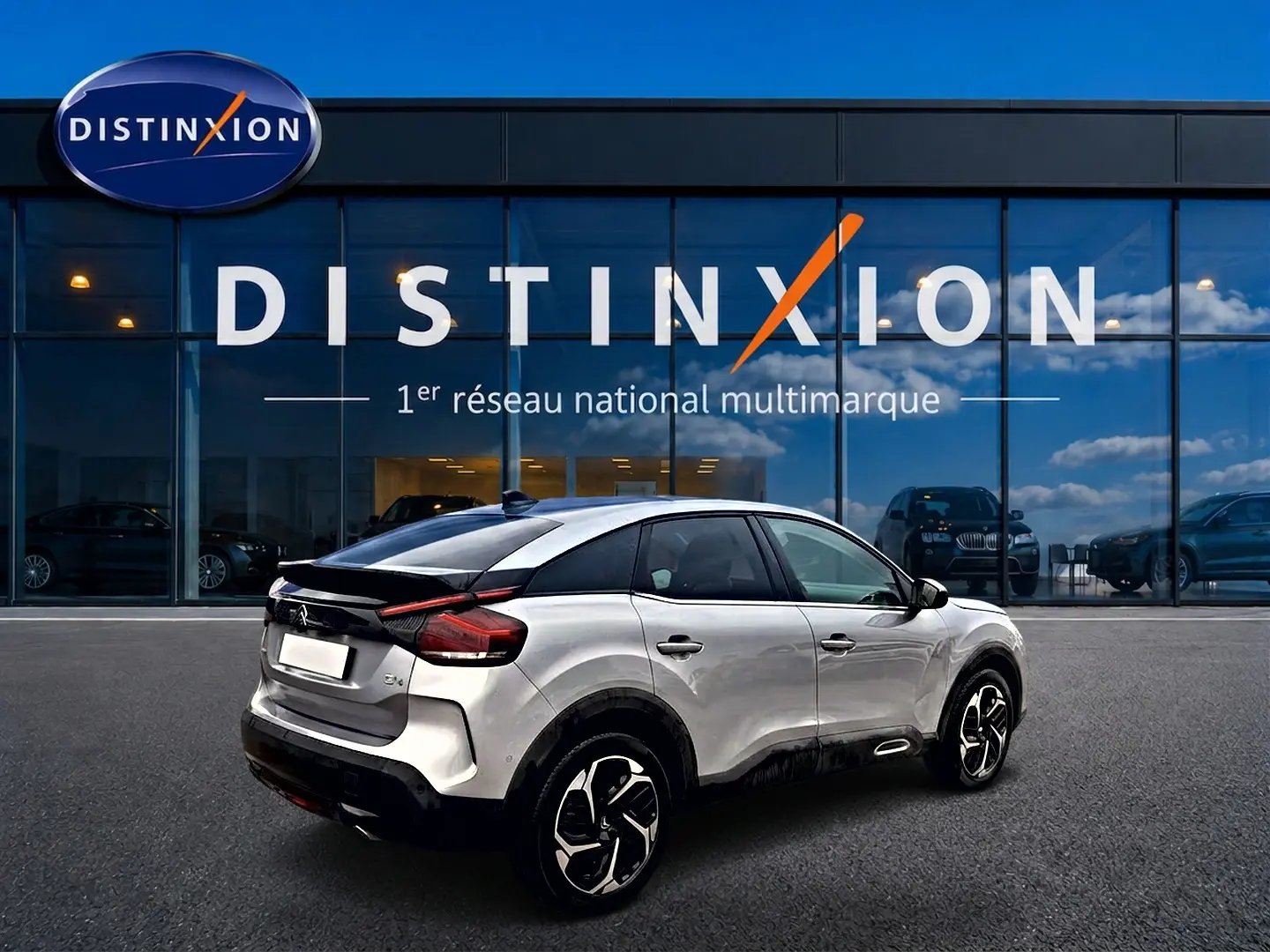 Citroën C4 gris vue 3/4 arrière droit, avec jantes alu noires et toit noir devant un showroom Distinxion.