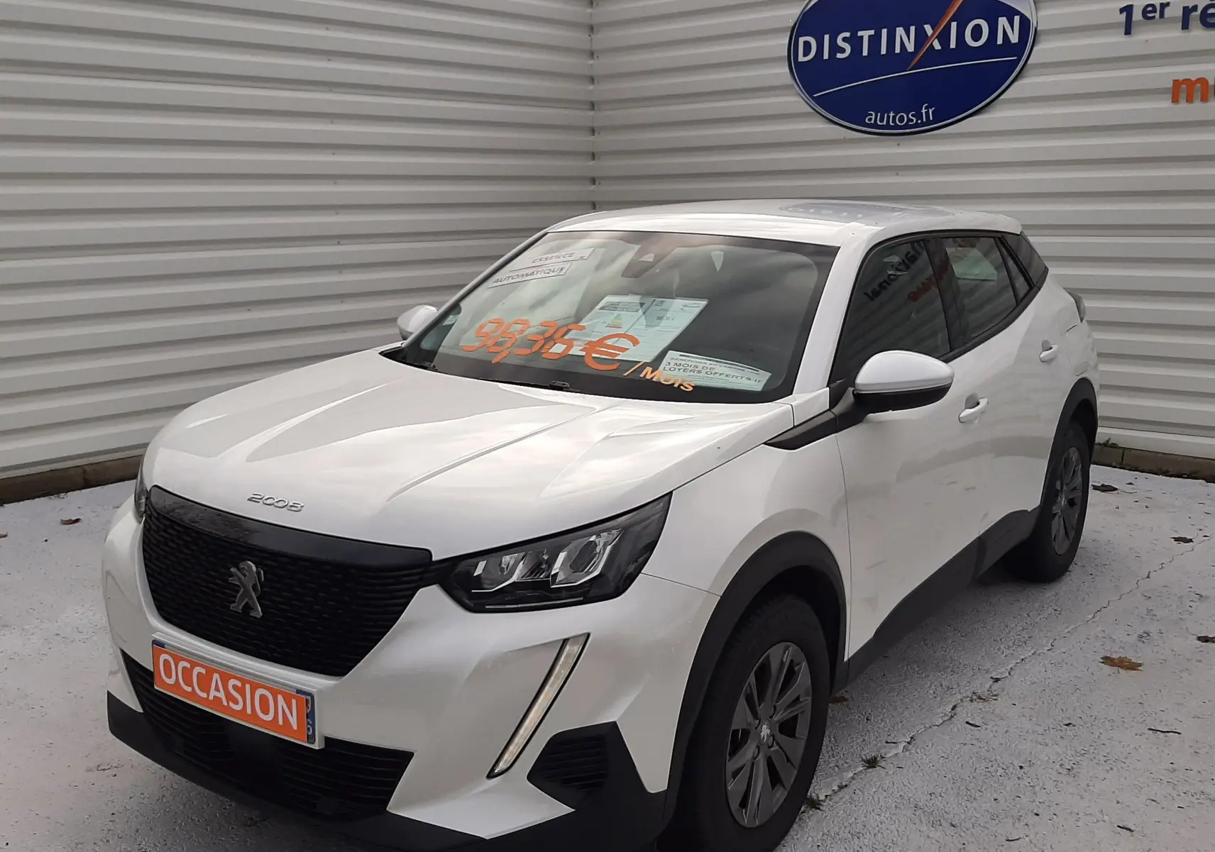 Peugeot 2008 blanc en 3/4 avant droit, avec calandre noire et feux LED, stationné devant un mur gris.