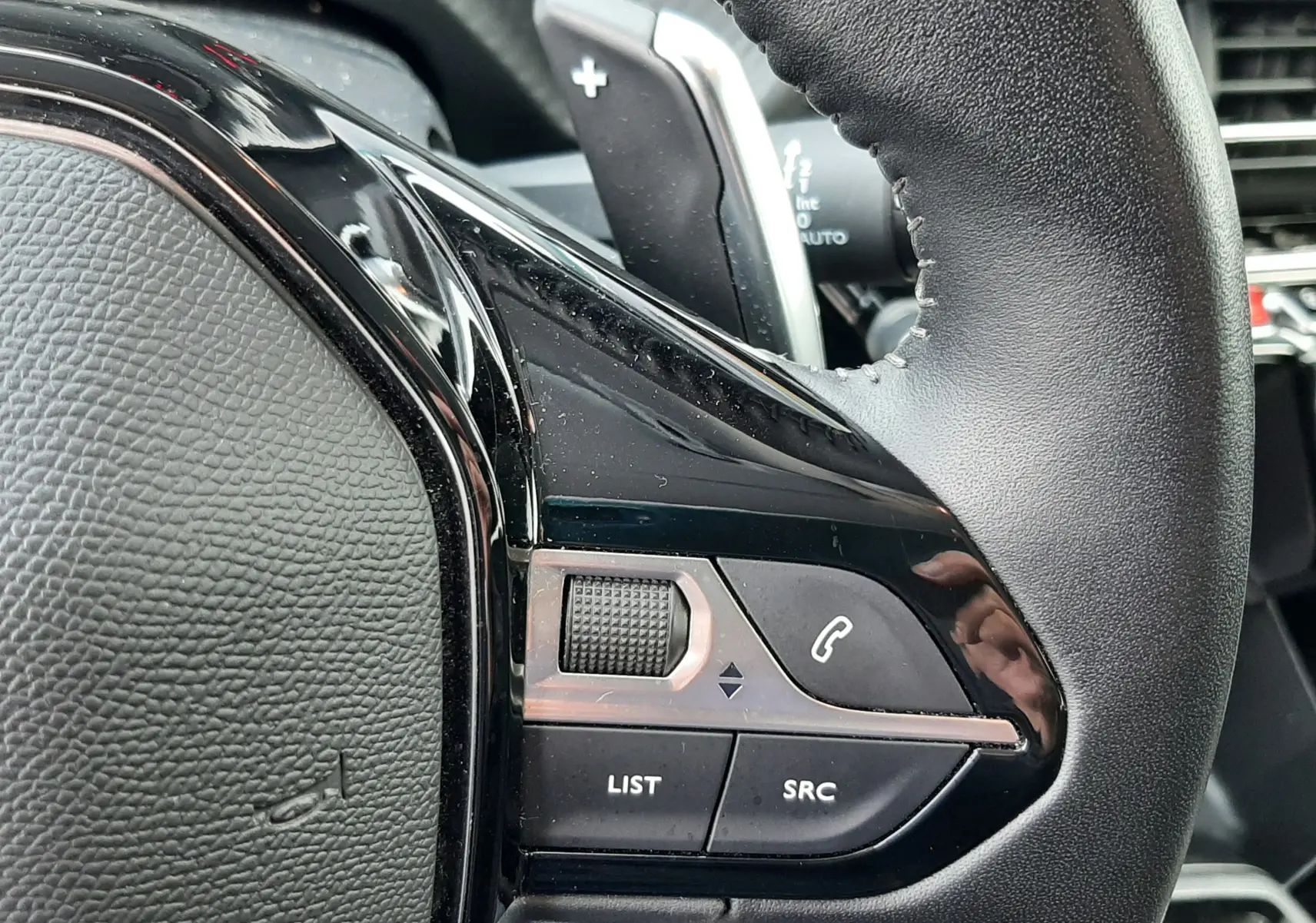 Gros plan sur le volant noir d'une Peugeot 2008 2021, montrant les commandes audio et la palette de changement de vitesses.