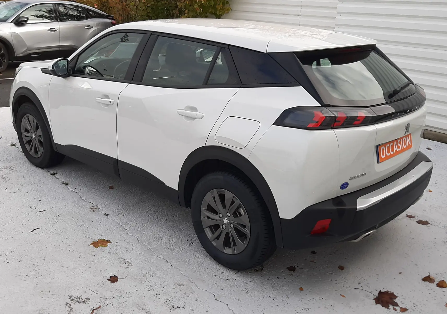 Peugeot 2008 blanc vue 3/4 arrière côté gauche, avec toit noir et feux arrière LED distinctifs.