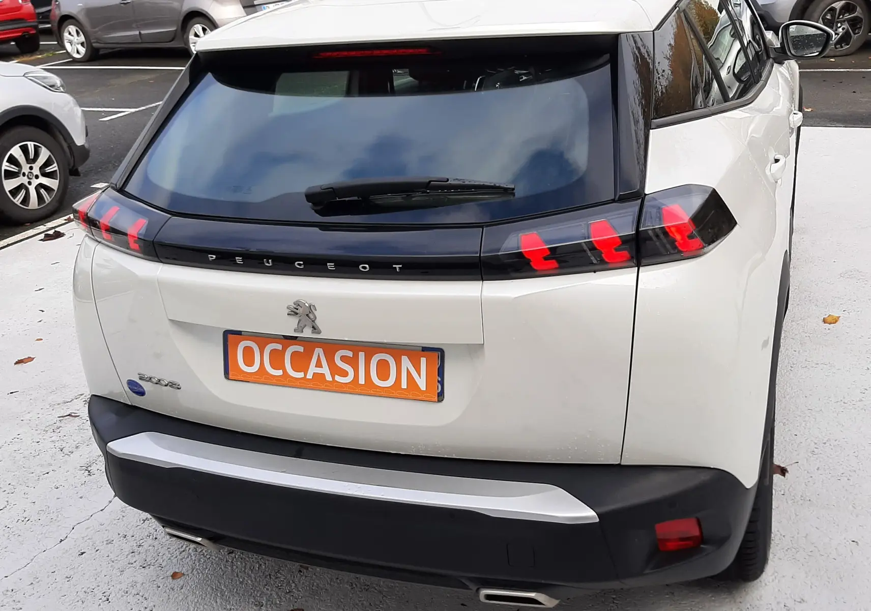 Vue 3/4 arrière droite d’un Peugeot 2008 blanc avec feux arrière à griffes rouges et plaque "OCCASION".