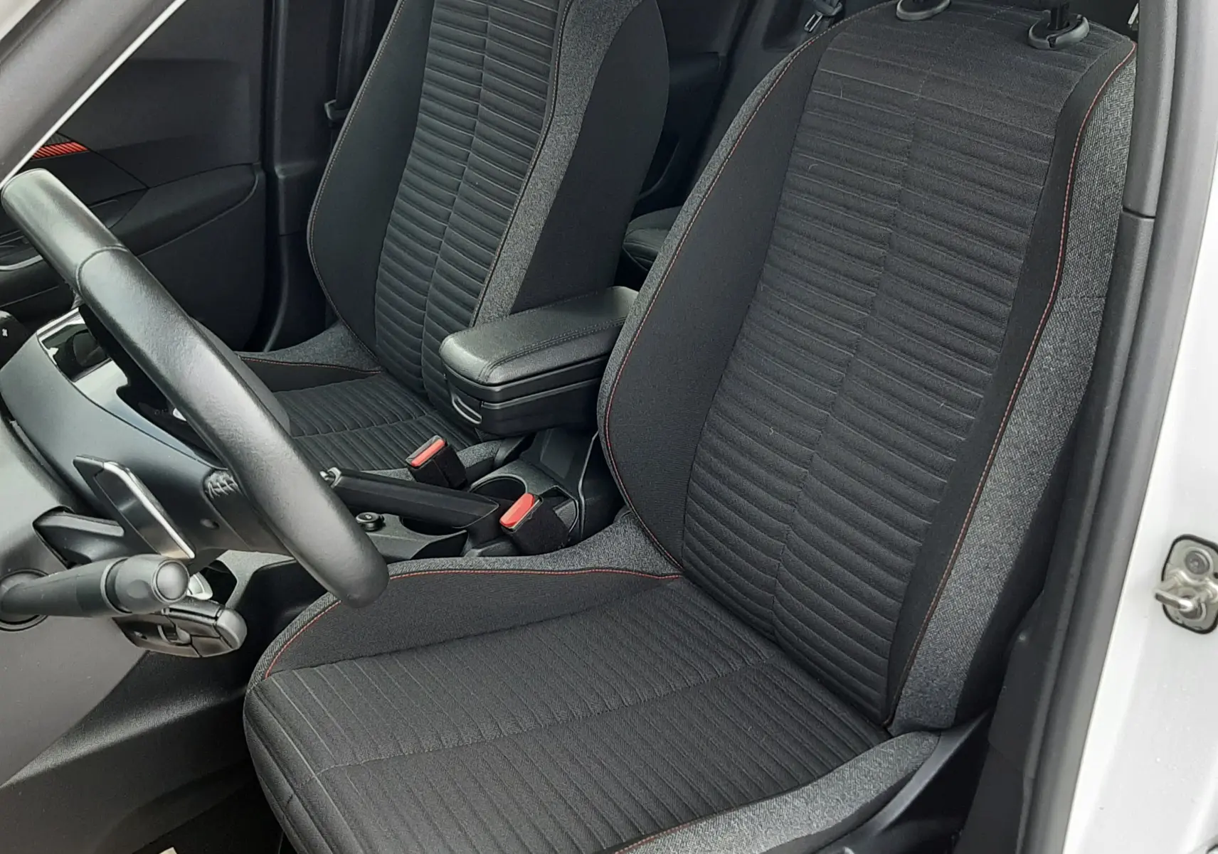 Vue intérieure côté conducteur du Peugeot 2008 blanc 2021, sièges tissu noir avec surpiqûres rouges et accoudoir central.