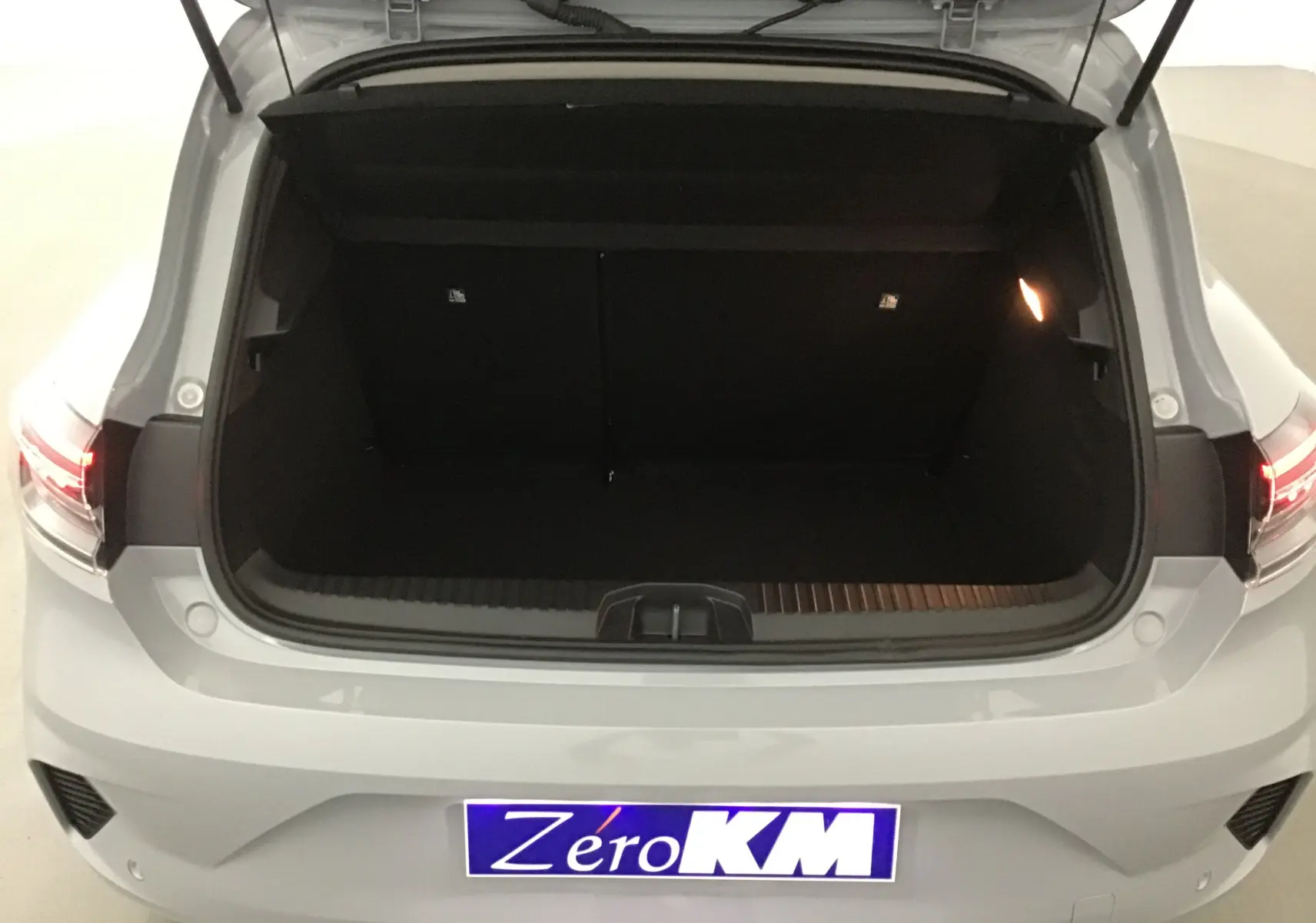Coffre ouvert vu de l'arrière d'une Renault Clio V gris Rafale, avec feux arrière allumés et plaque Zero KM.