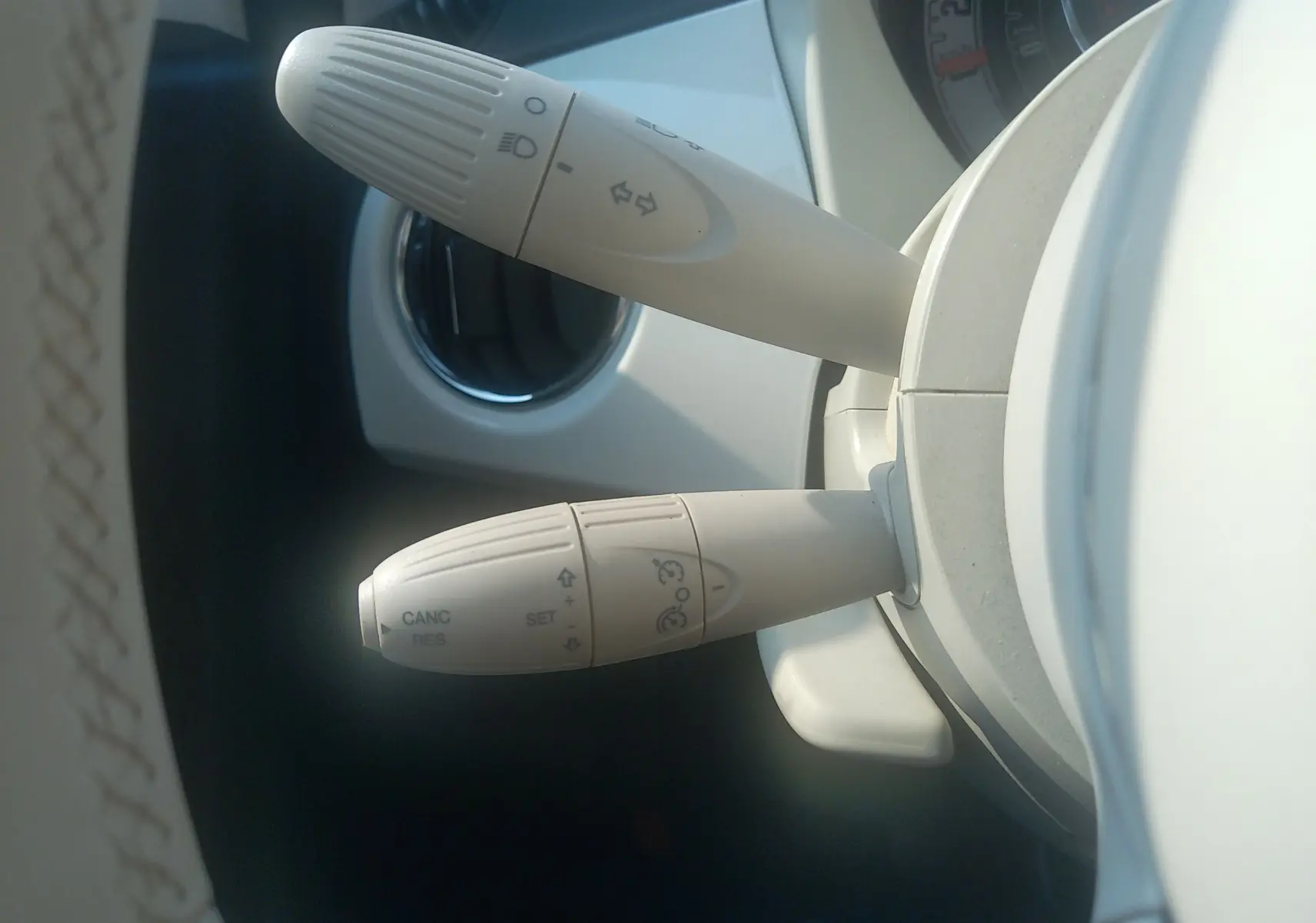 Gros plan sur les commandes blanches du volant d'une Fiat 500 blanche, montrant les leviers de clignotants et régulateur de vitesse.