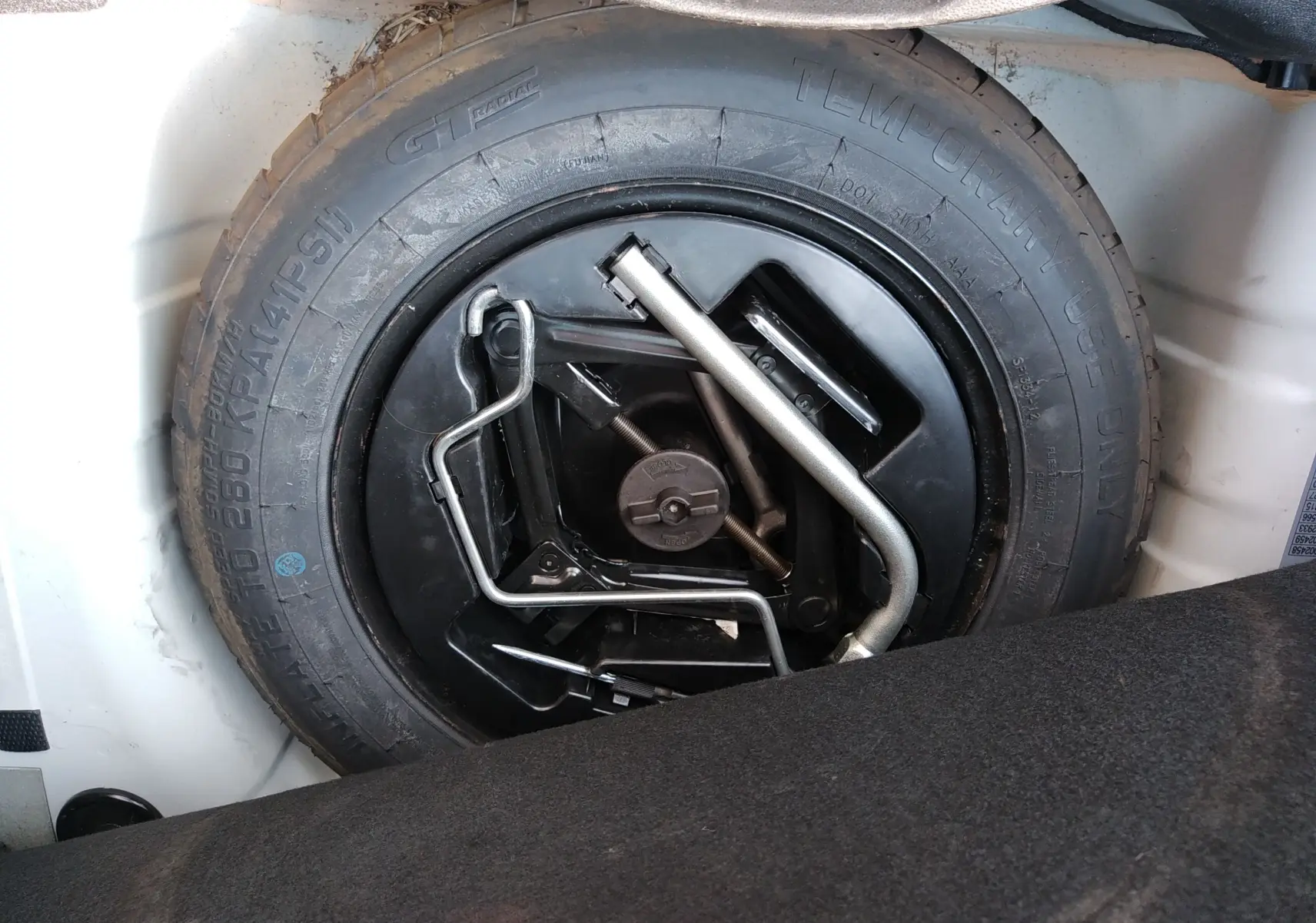 Roue de secours noire avec outils de changement dans le coffre d'une Fiat 500 blanche hybride 2021.