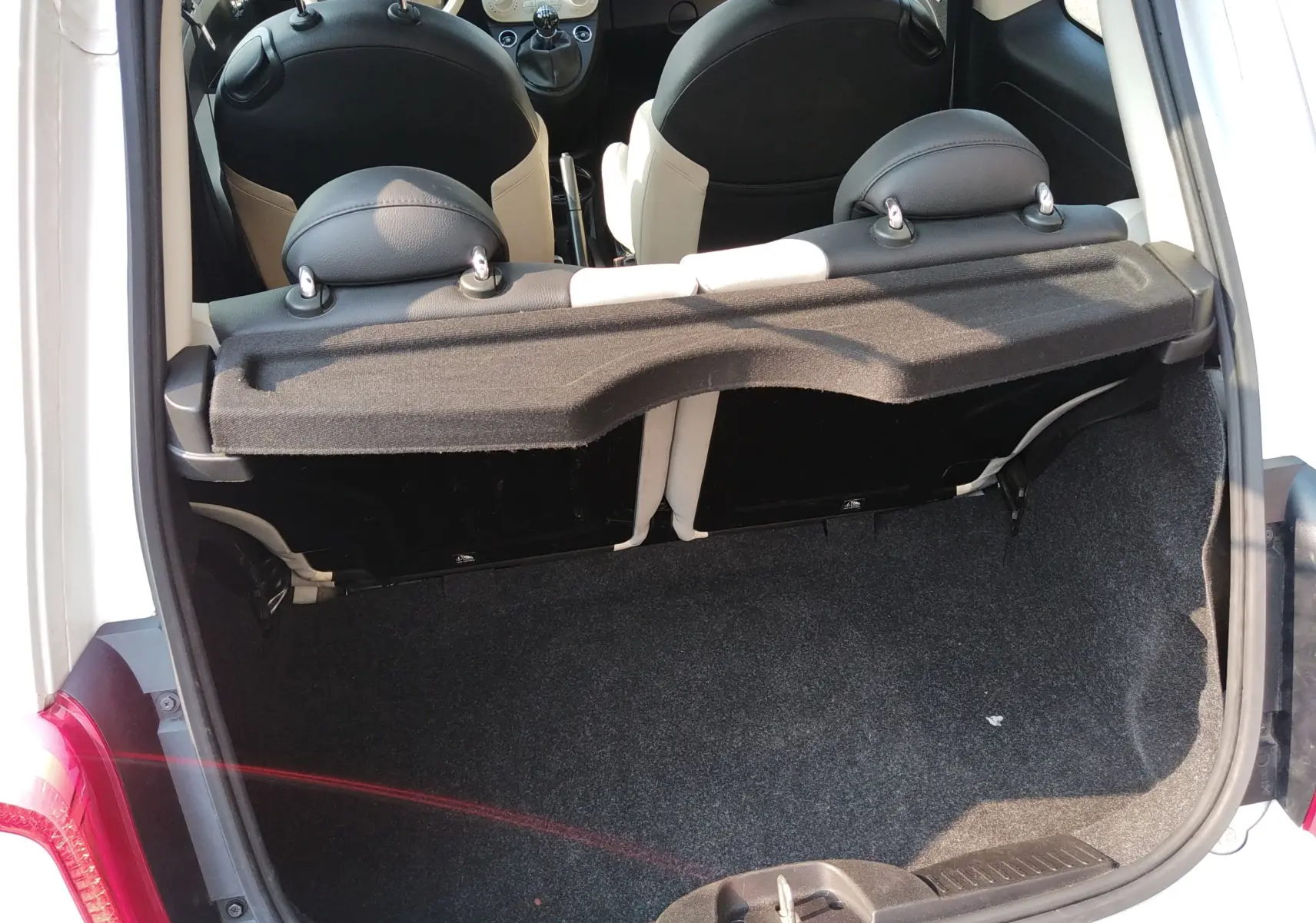 Coffre ouvert vu de l'arrière d'une FIAT 500 blanche, montrant l'intérieur noir et blanc des sièges arrière.