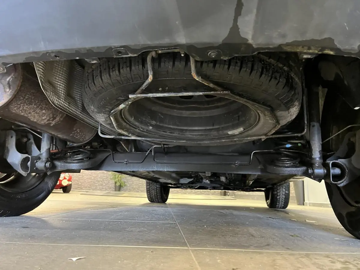 Vue en contre-plongée sous un Dacia Duster noir 2016 montrant la roue de secours fixée sous le véhicule.