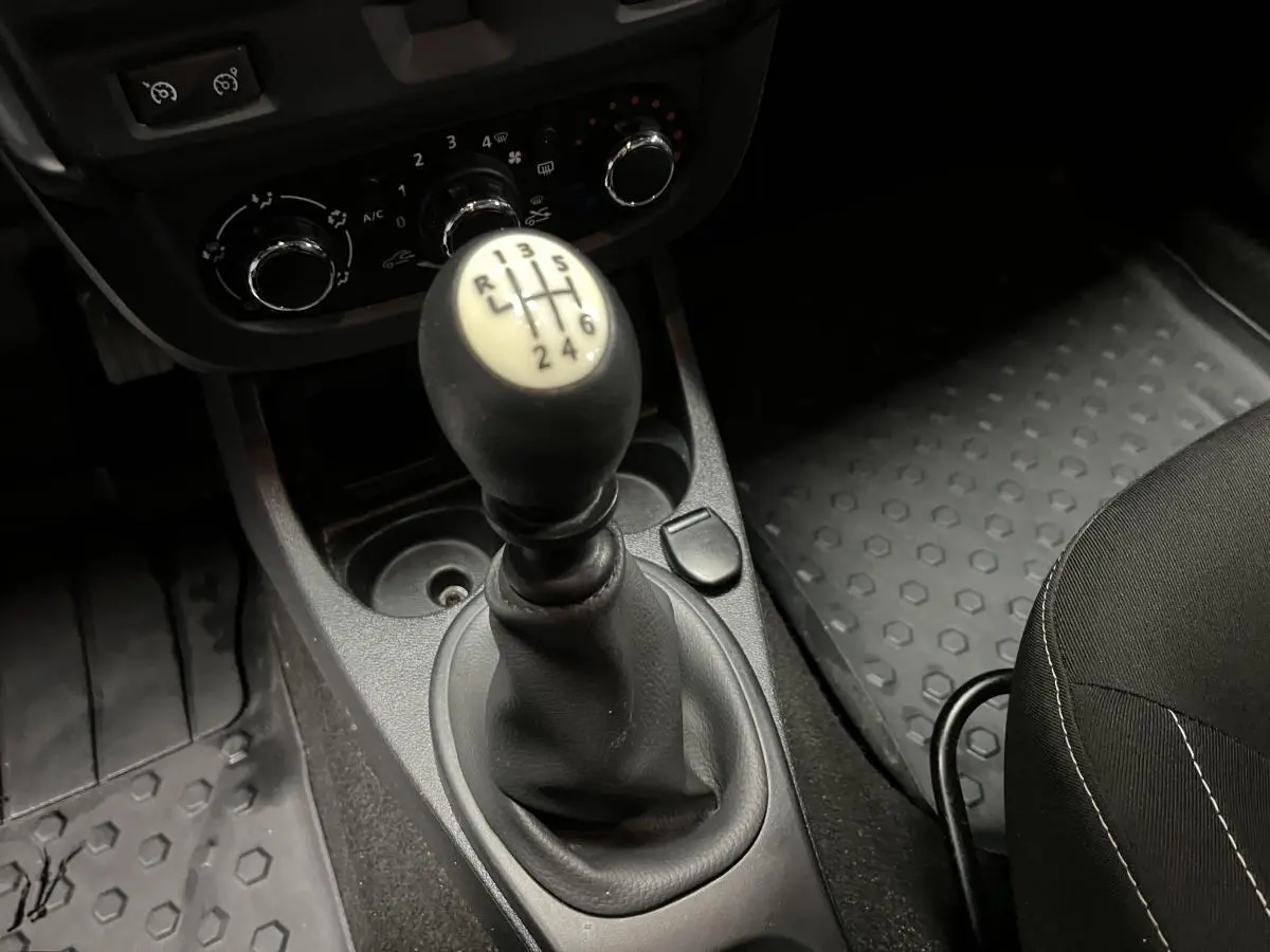 Le levier de vitesses manuel noir et beige du Dacia Duster 2016, entouré de commandes de climatisation et tapis caoutchouc.