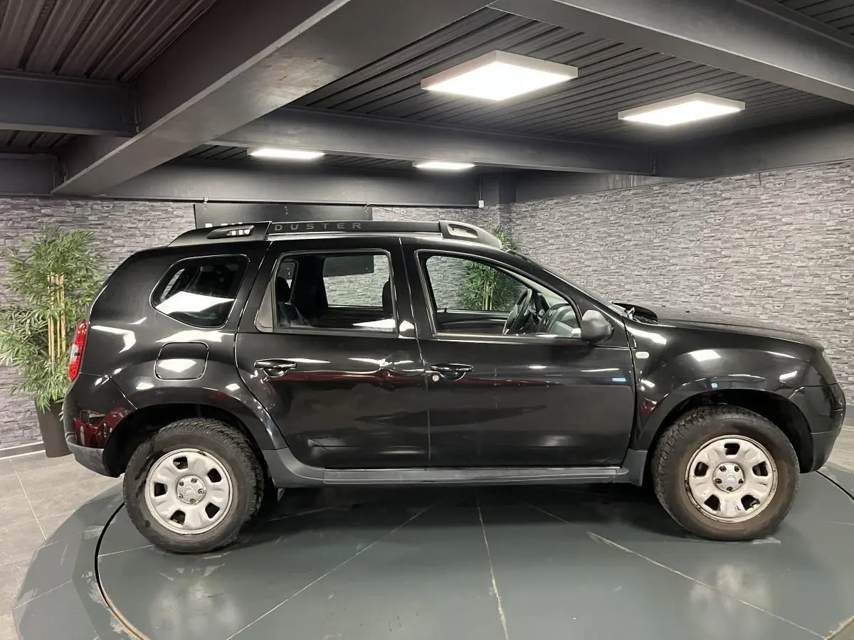Profil côté gauche d'un Dacia Duster noir 2016 avec barres de toit et jantes acier 16 pouces en intérieur.