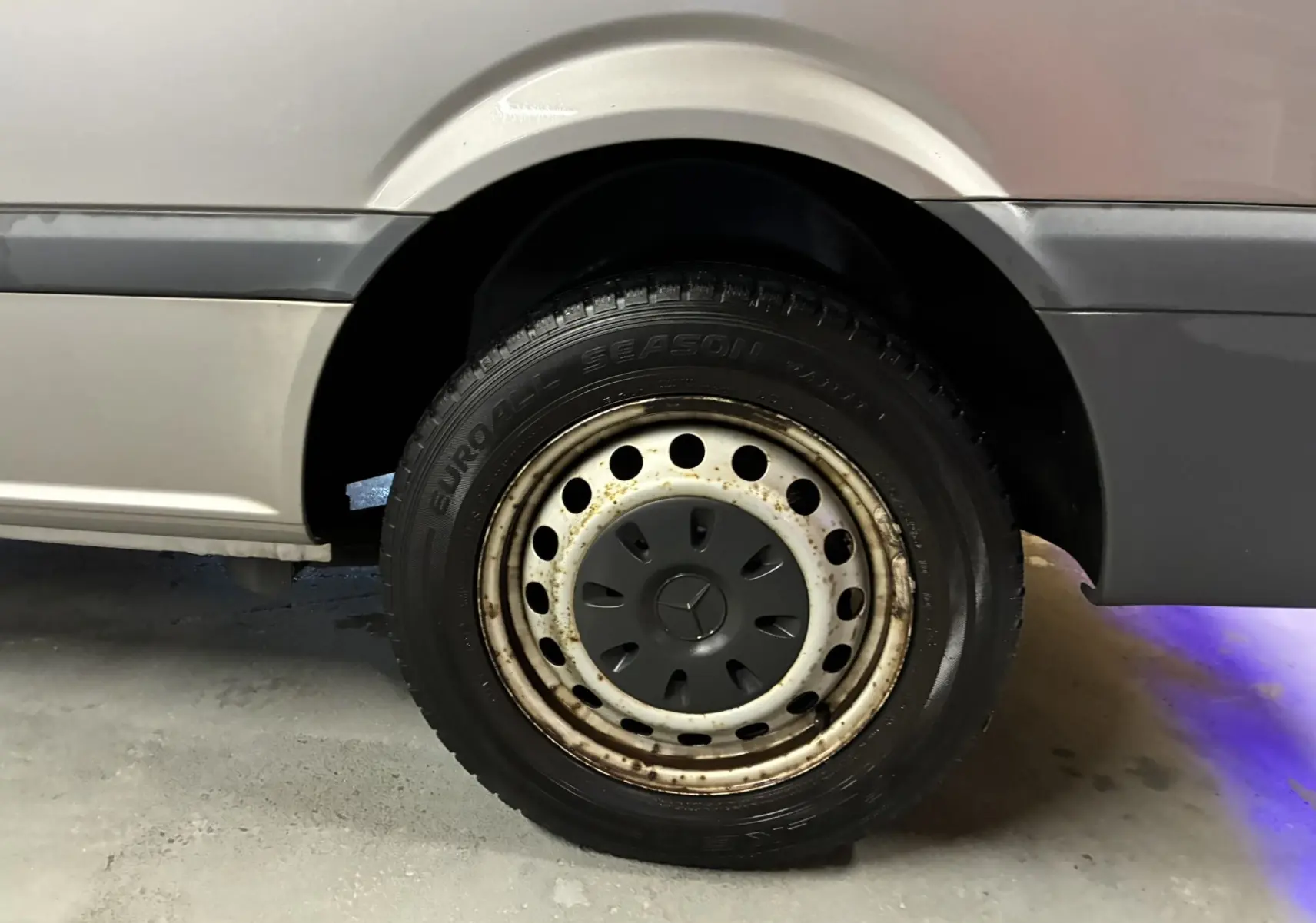 Gros plan sur la roue arrière droite grise d’un Mercedes Vito 2.8 113 CDI Fourgon Long avec jante acier et logo Mercedes central.