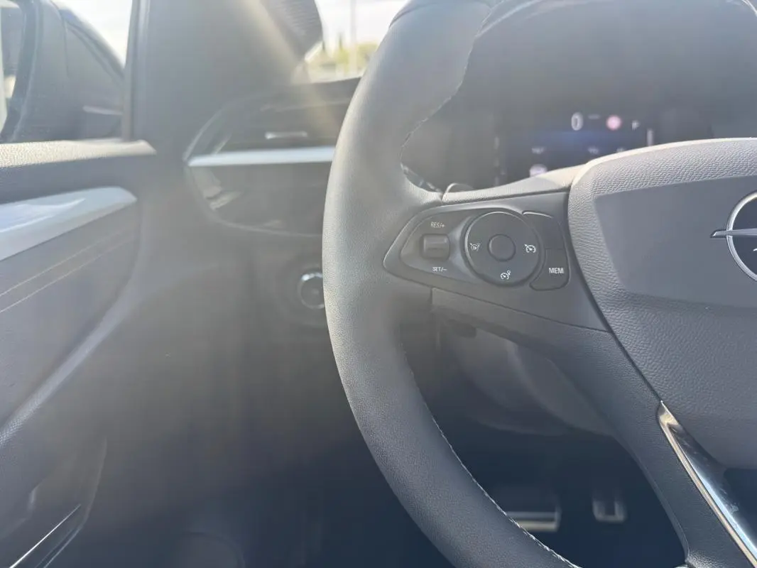 Vue intérieure côté gauche du volant noir d'une Opel Corsa 2025, avec commandes au volant et tableau de bord partiellement visible.