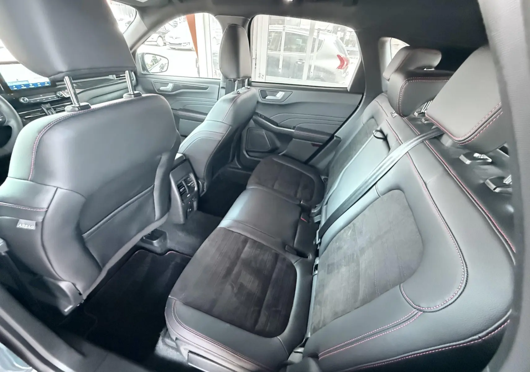 Vue intérieure arrière côté droit du Ford Kuga 2023, sièges cuir noir avec surpiqûres rouges et finitions ST-Line.