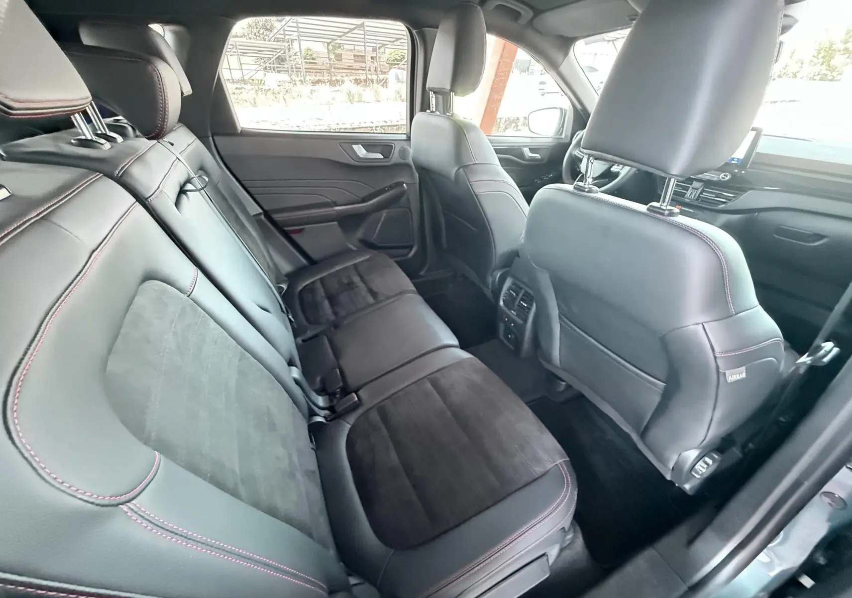 Vue intérieure arrière du Ford Kuga 2023 ST-Line X, sièges en cuir noir avec surpiqûres rouges et inserts alcantara.