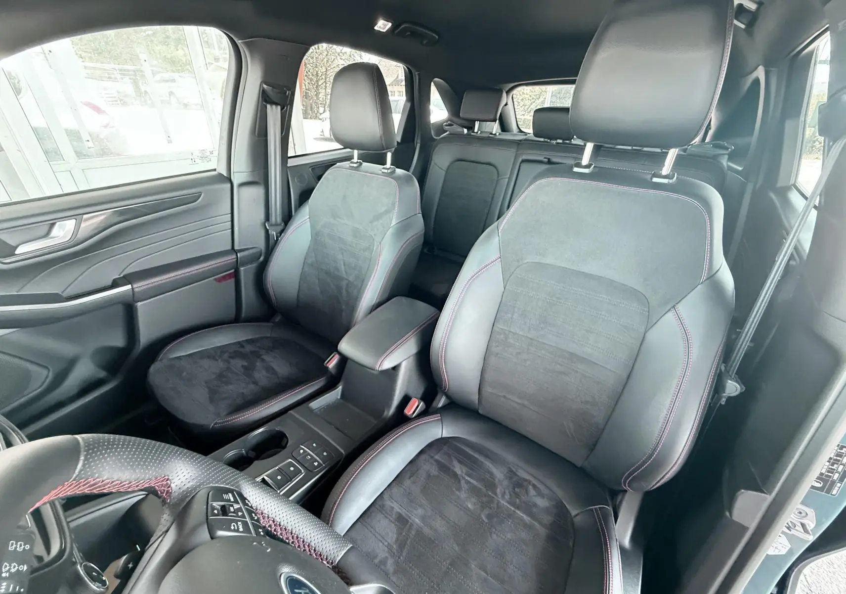 Vue intérieure avant du Ford Kuga 2023 avec sièges ST-Line en cuir noir et surpiqûres rouges, volant méplat visible.