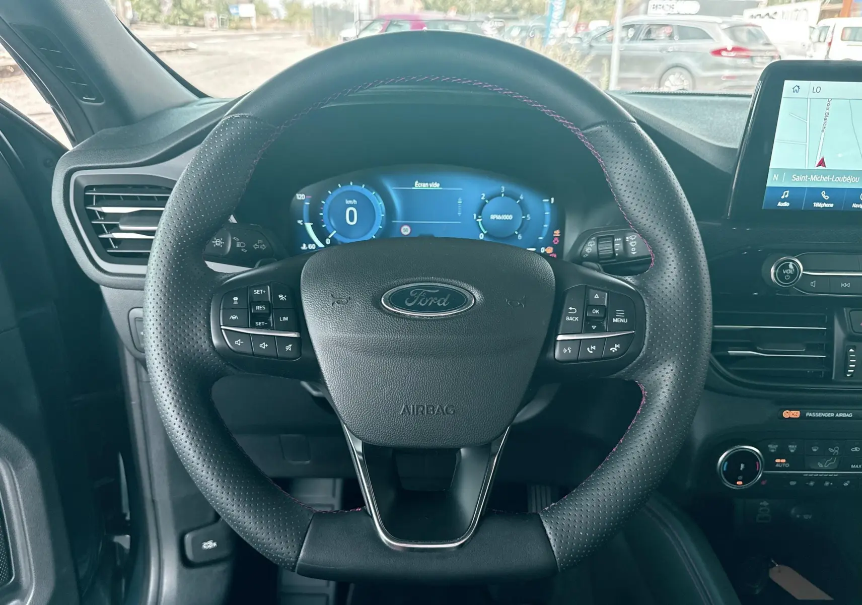 Vue intérieure centrée sur le volant perforé noir avec surpiqûres rouges du Ford Kuga 2023, tableau de bord numérique et écran tactile visibles.