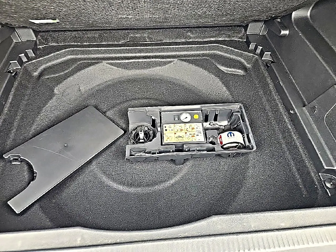Vue plongeante sur le coffre du Citroën C5 Aircross gris, montrant le rangement sous plancher avec kit de réparation pneus.