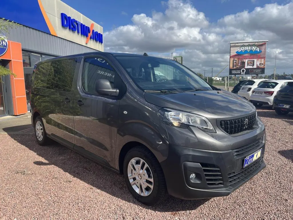 Peugeot Expert Fourgon gris platinium métal en 3/4 avant droit, stationné devant un bâtiment commercial.