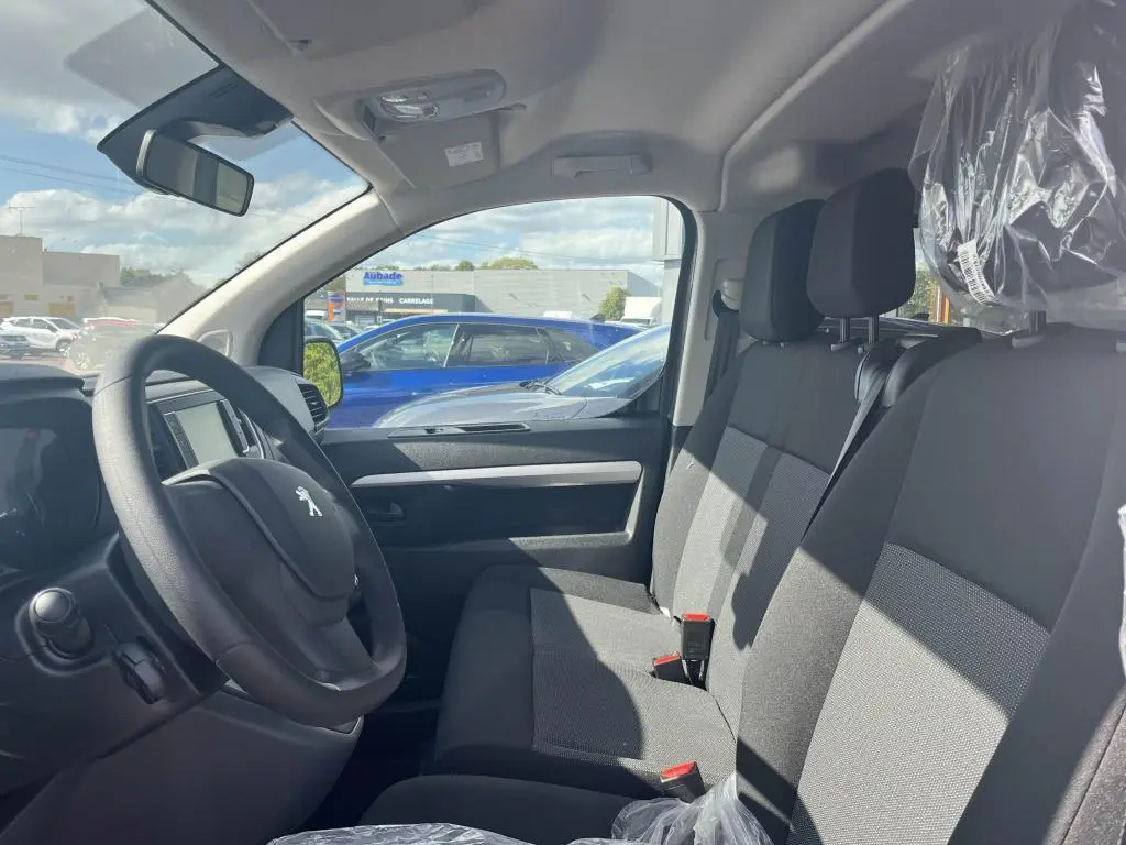Vue intérieure côté conducteur du Peugeot Expert Fourgon 2023, sièges tissu gris et volant avec logo lion visible.