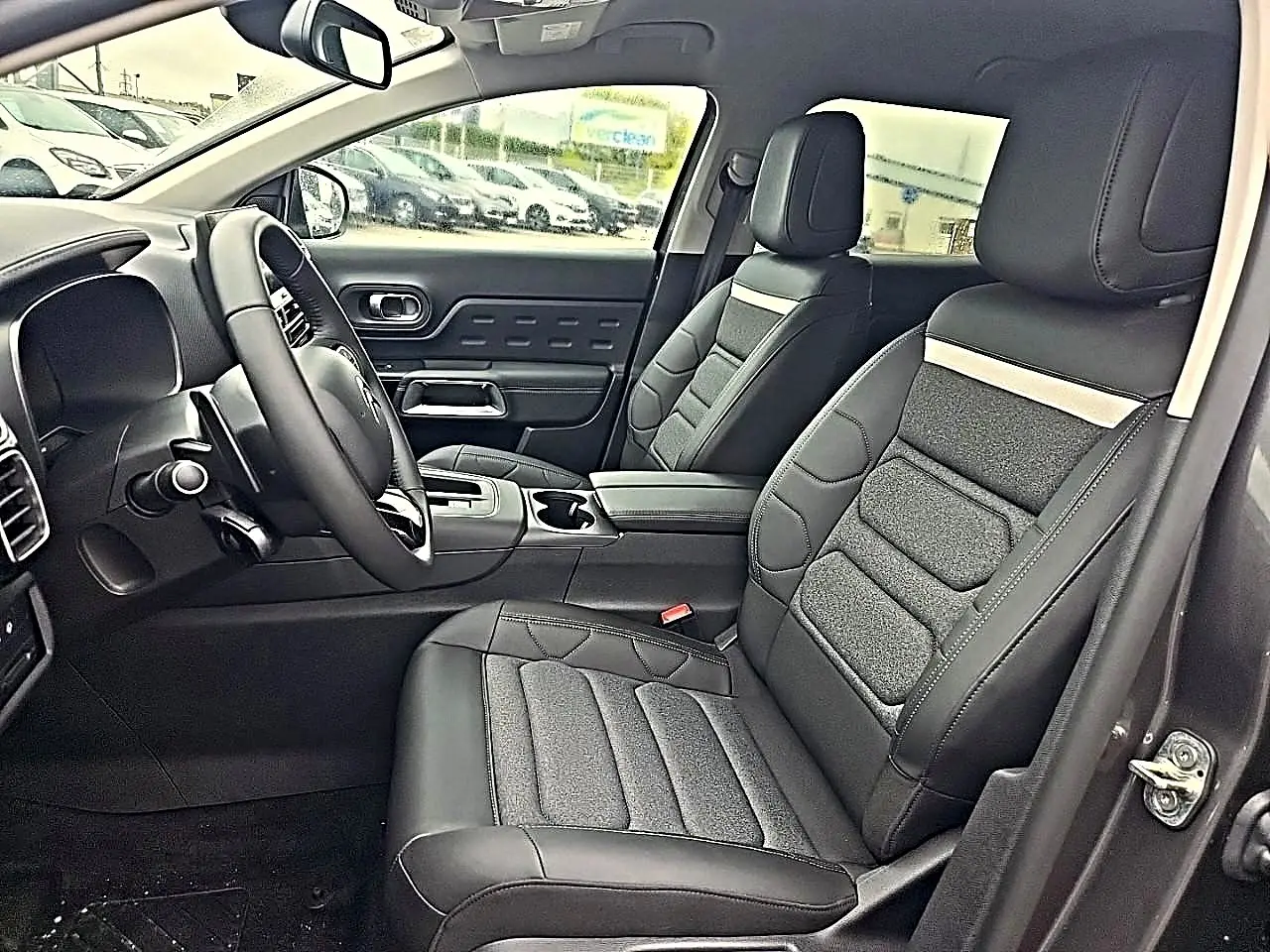 Vue intérieure côté conducteur du Citroën C5 Aircross gris 2025, sièges noirs en cuir et tissu avec console centrale.