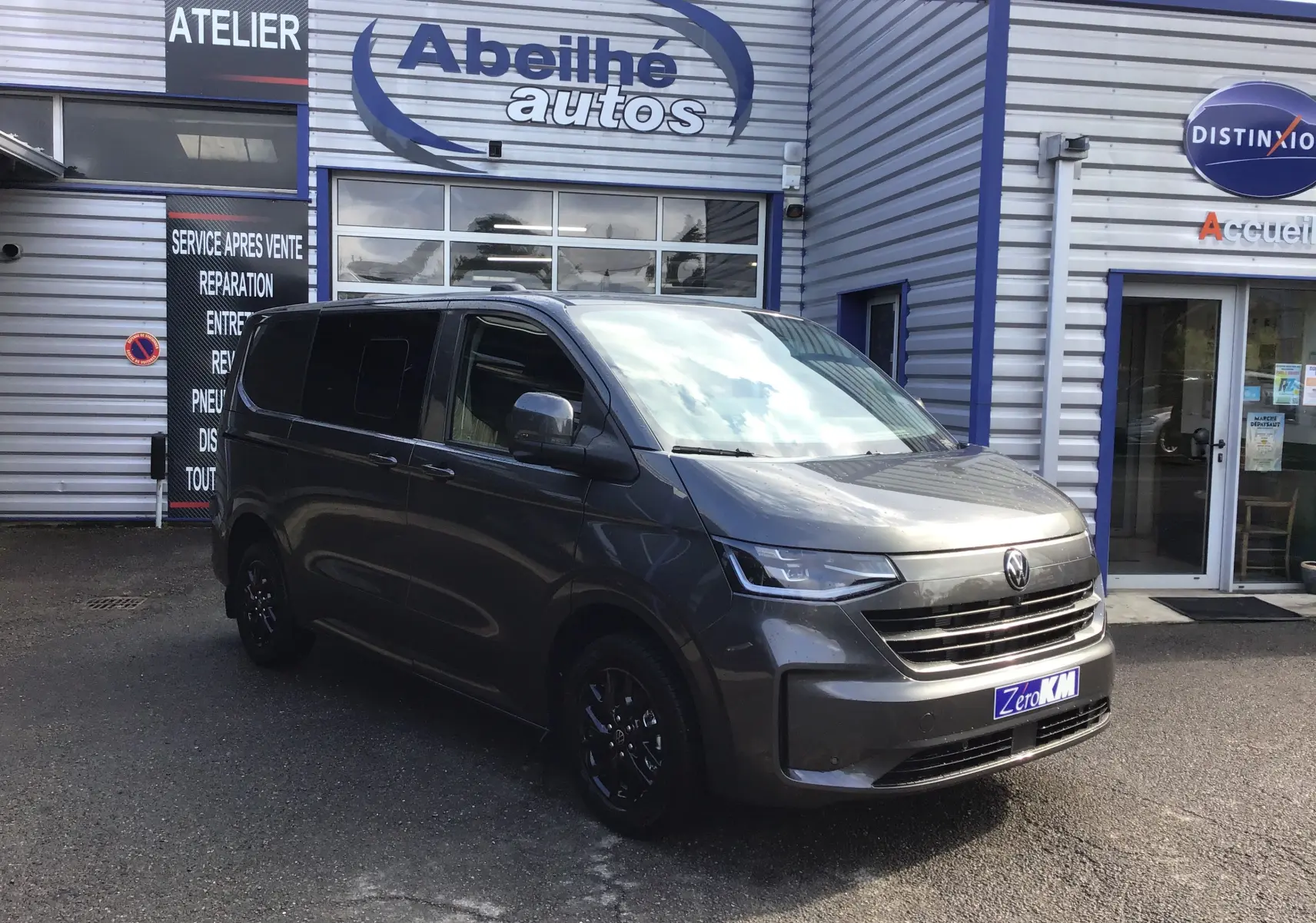Vue 3/4 avant d'un Volkswagen Transporter ProCab gris anthracite avec jantes alu noires devant un garage Abeillé autos.