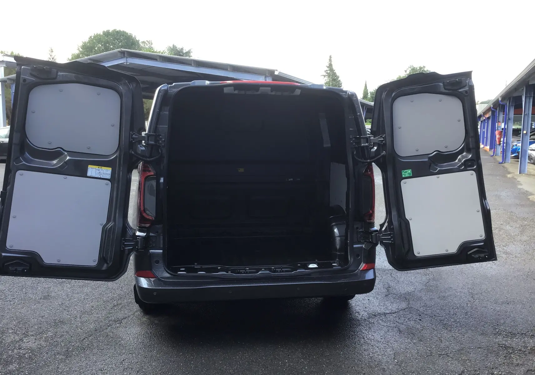Vue arrière du Volkswagen Transporter ProCab gris anthracite 2025 avec portes battantes ouvertes dévoilant le compartiment de charge vide.