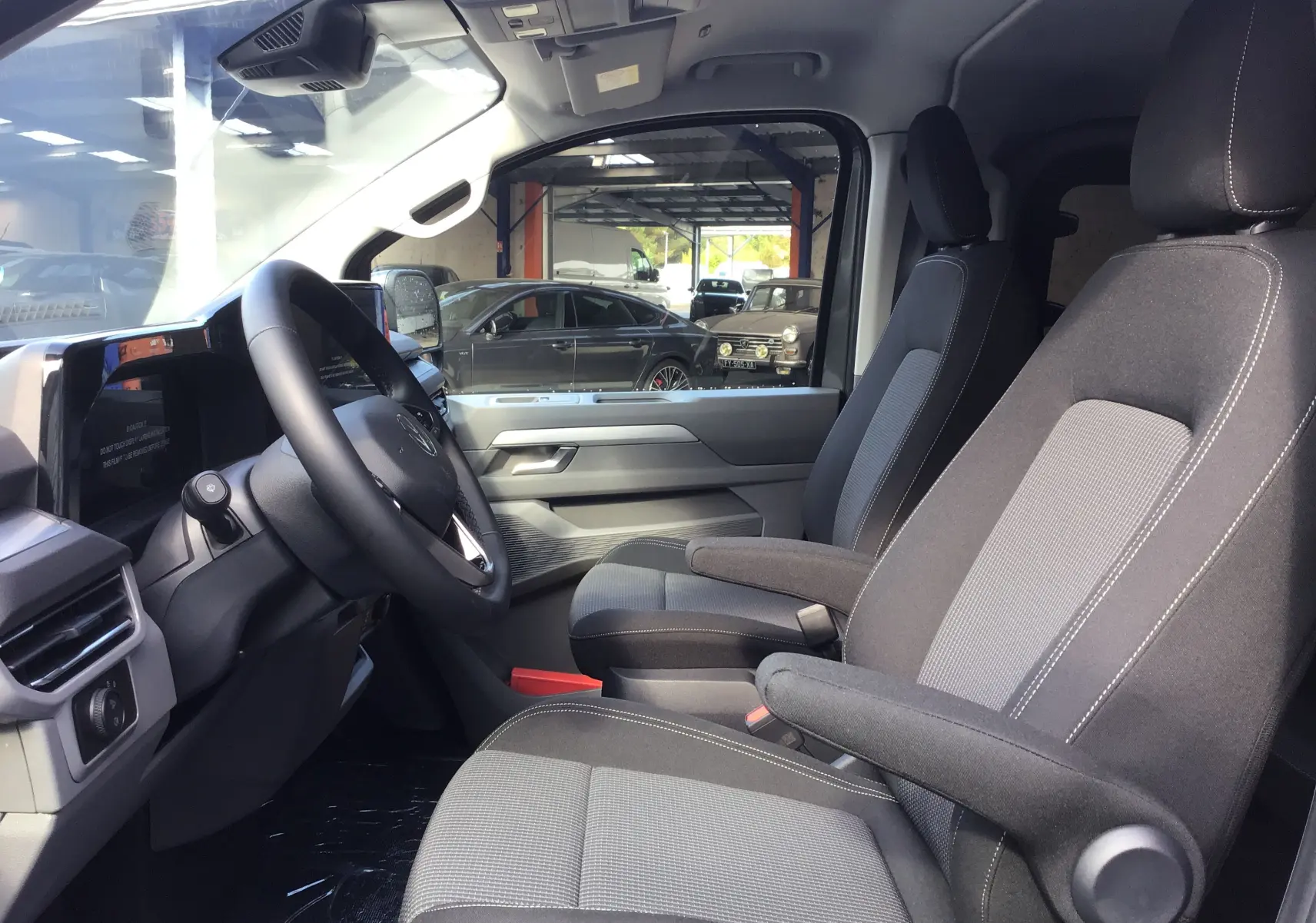 Intérieur avant du Volkswagen Transporter ProCab 2025 gris anthracite, sièges tissu gris avec accoudoirs et tableau de bord moderne.