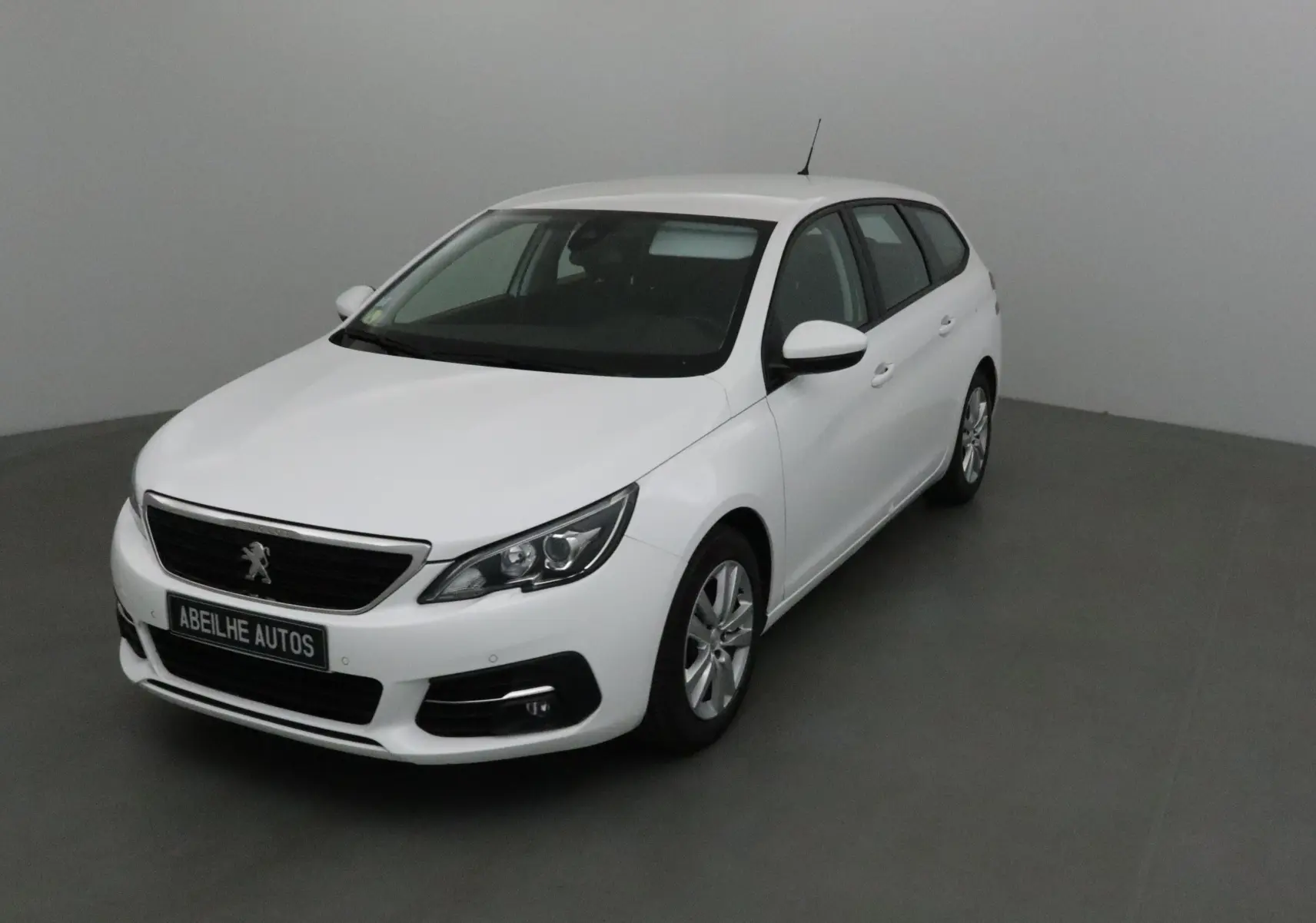 Peugeot 308 SW blanche vue en 3/4 avant droit dans un intérieur neutre avec jantes alliage et calandre noire.