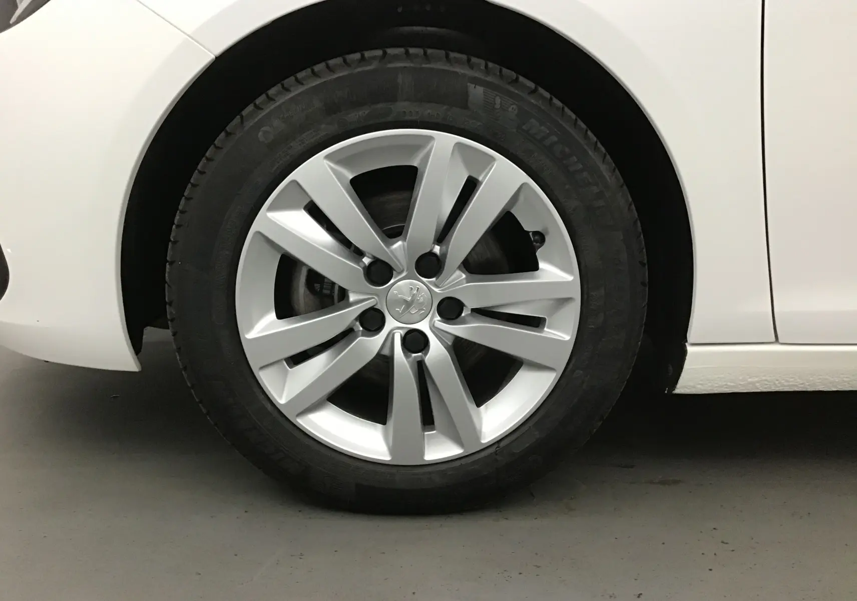 Gros plan sur la roue avant gauche d'une Peugeot 308 SW blanche de 2018 avec jante alliage 16 pouces.