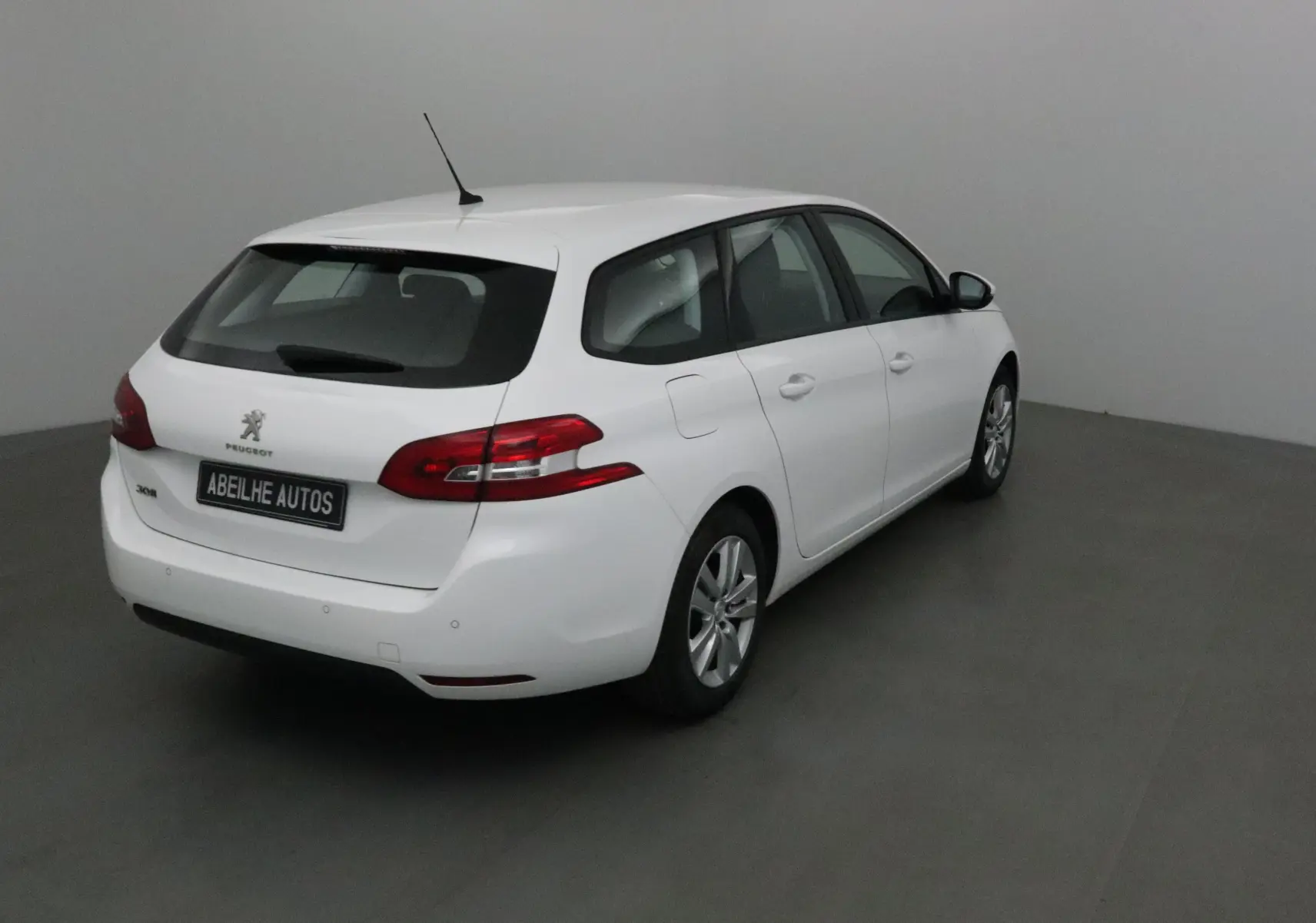 Peugeot 308 SW blanche vue 3/4 arrière droit dans un intérieur neutre avec feux arrière rouges distinctifs.