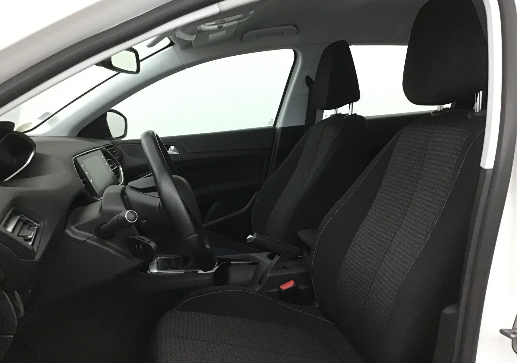 Intérieur côté conducteur d'une Peugeot 308 SW blanche 2018, montrant sièges noirs et tableau de bord moderne.