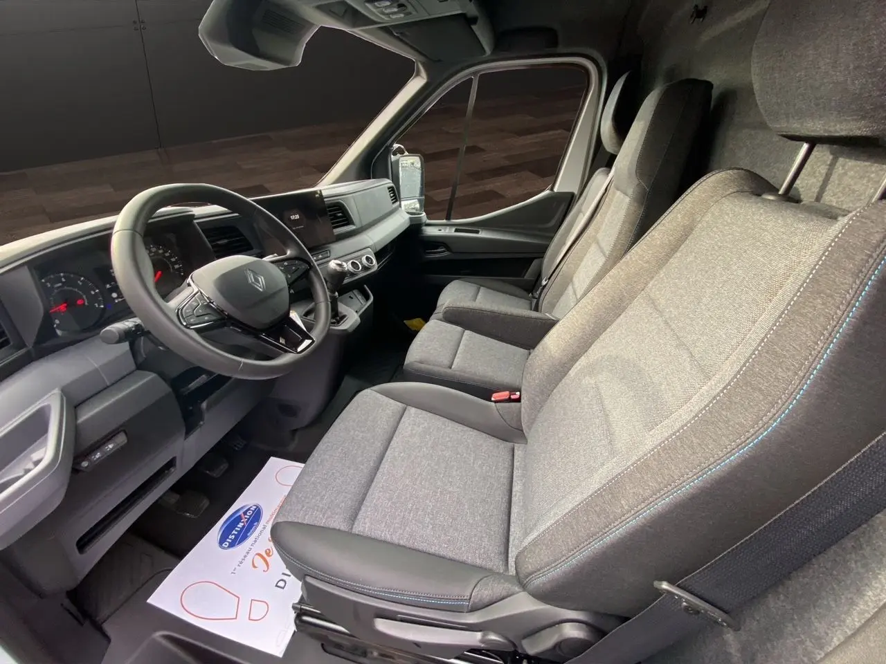 Vue intérieure côté conducteur du Renault Master 2025, sièges gris tissu avec surpiqûres bleues et tableau de bord noir.