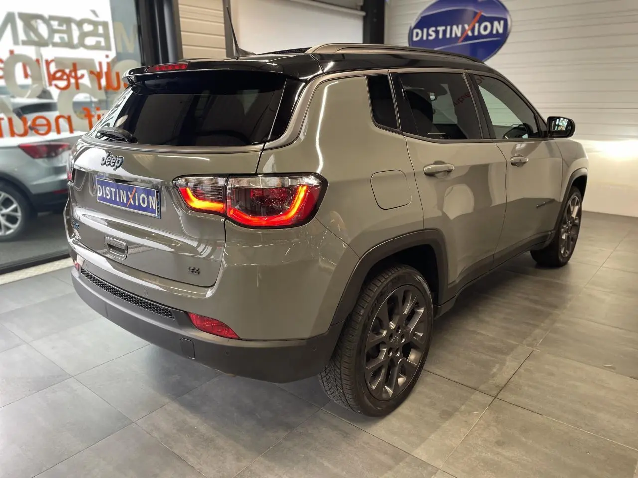Vue 3/4 arrière droit du Jeep Compass gris foncé avec feux arrière allumés et jantes alliage en showroom.