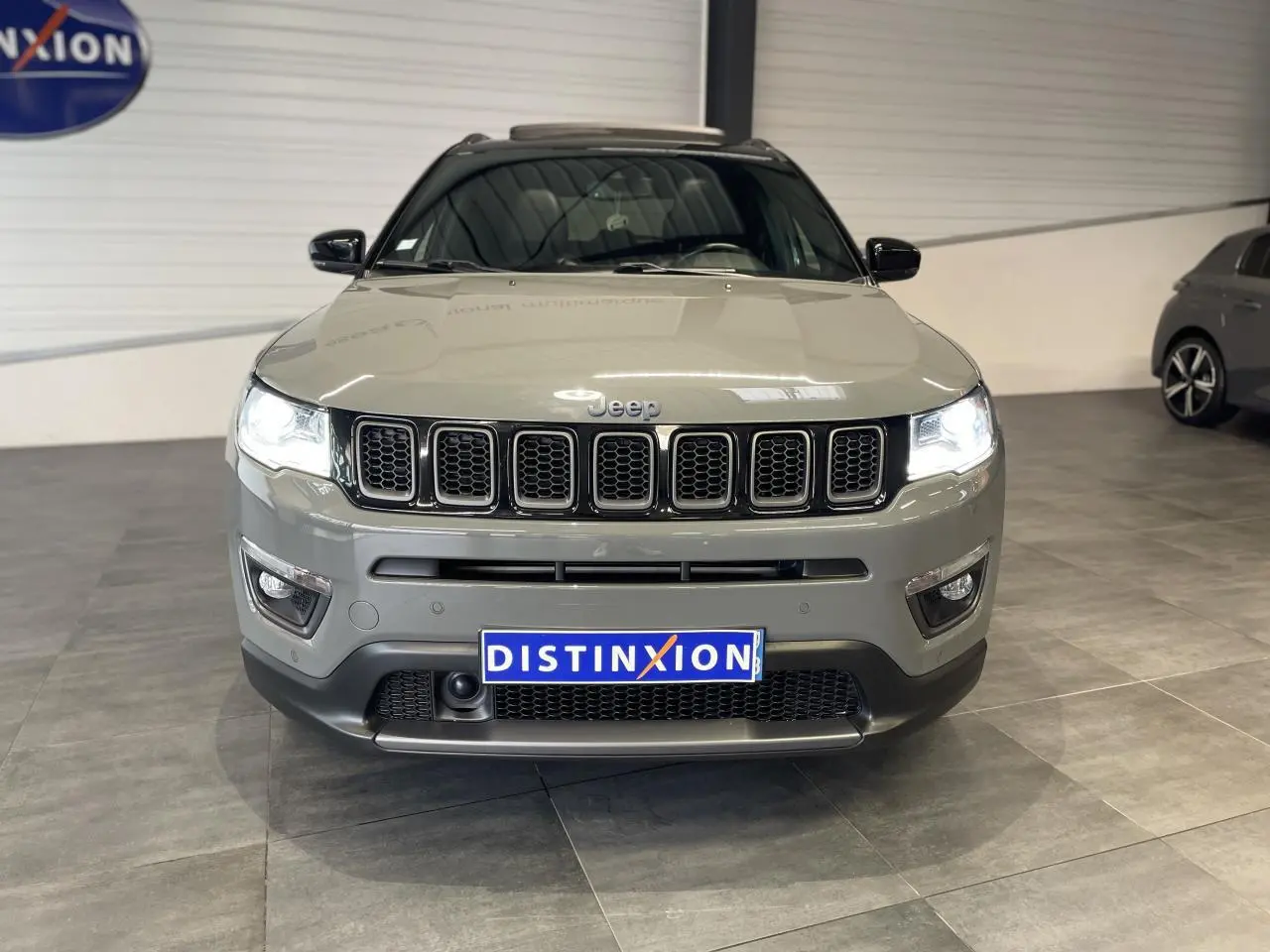 Jeep Compass gris foncé vue de face en intérieur, avec calandre à sept fentes et phares LED allumés.