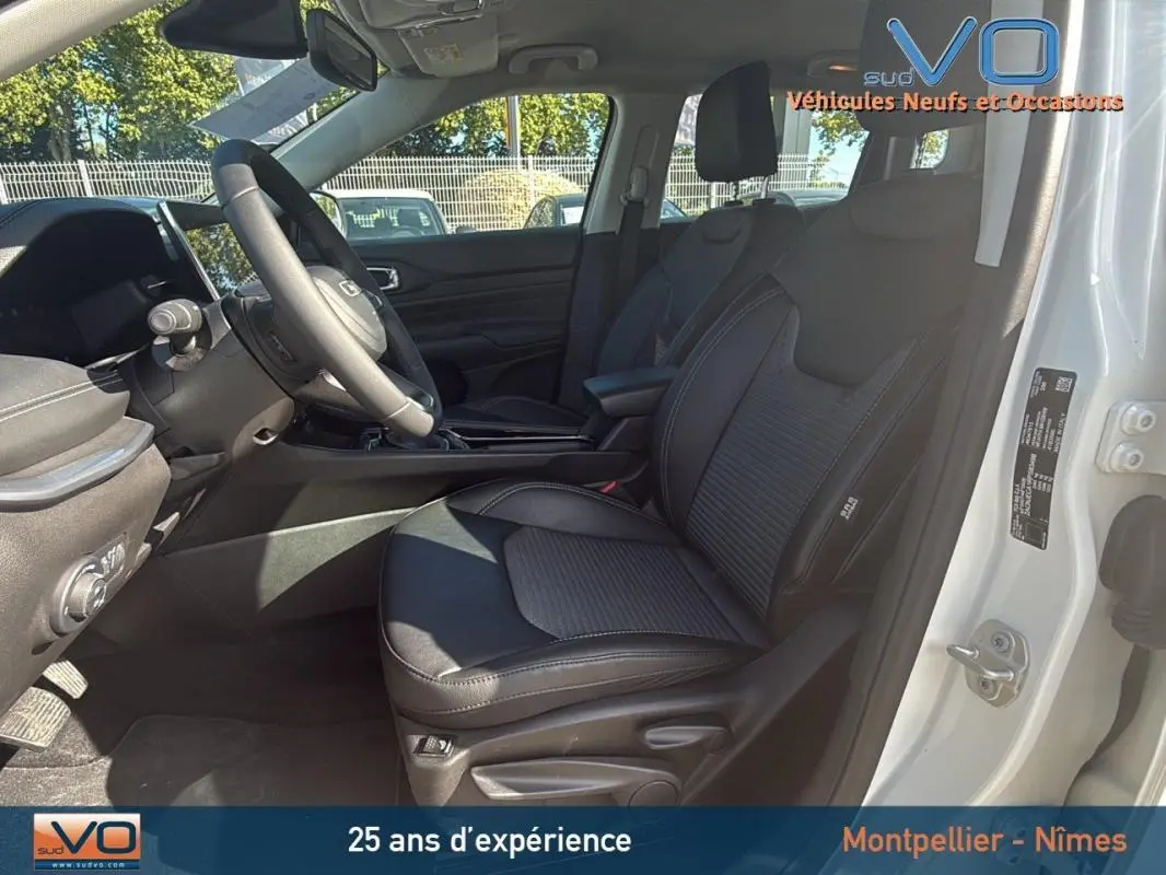 Intérieur noir du Jeep Compass 2024 blanc, vue côté conducteur ouverte montrant sièges et tableau de bord moderne.