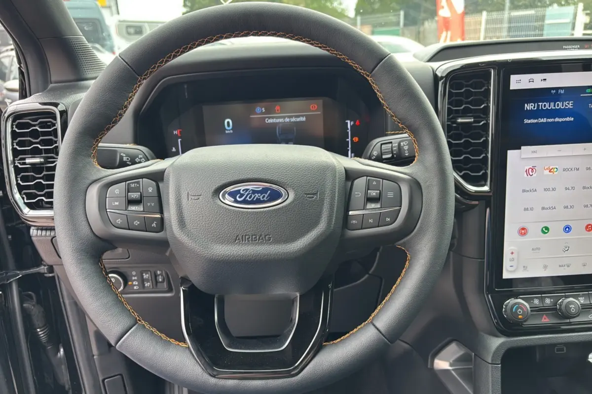 Vue rapprochée du volant cuir noir avec surpiqûres marron du Ford Ranger 2025, tableau de bord numérique et écran tactile visible.