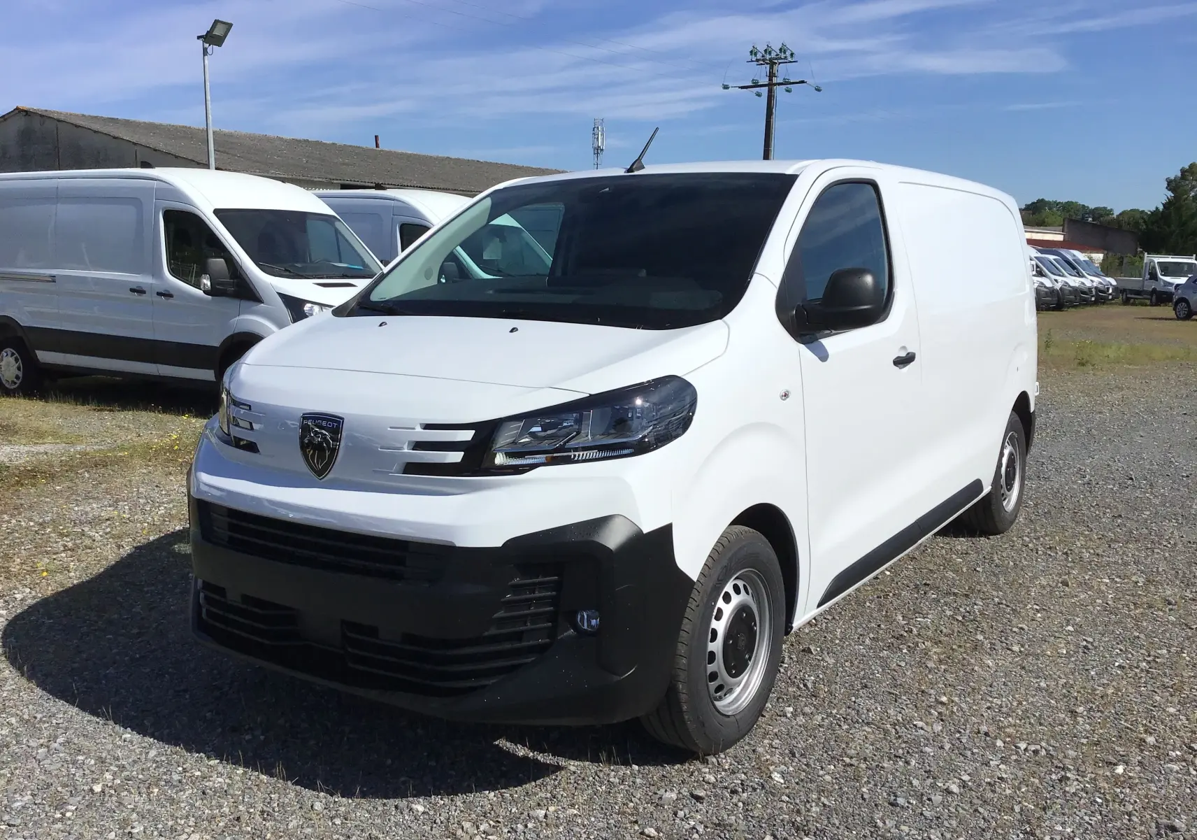 Fourgon Peugeot Expert blanc vu en 3/4 avant droit, avec calandre noire et jantes acier, stationné sur un terrain extérieur.