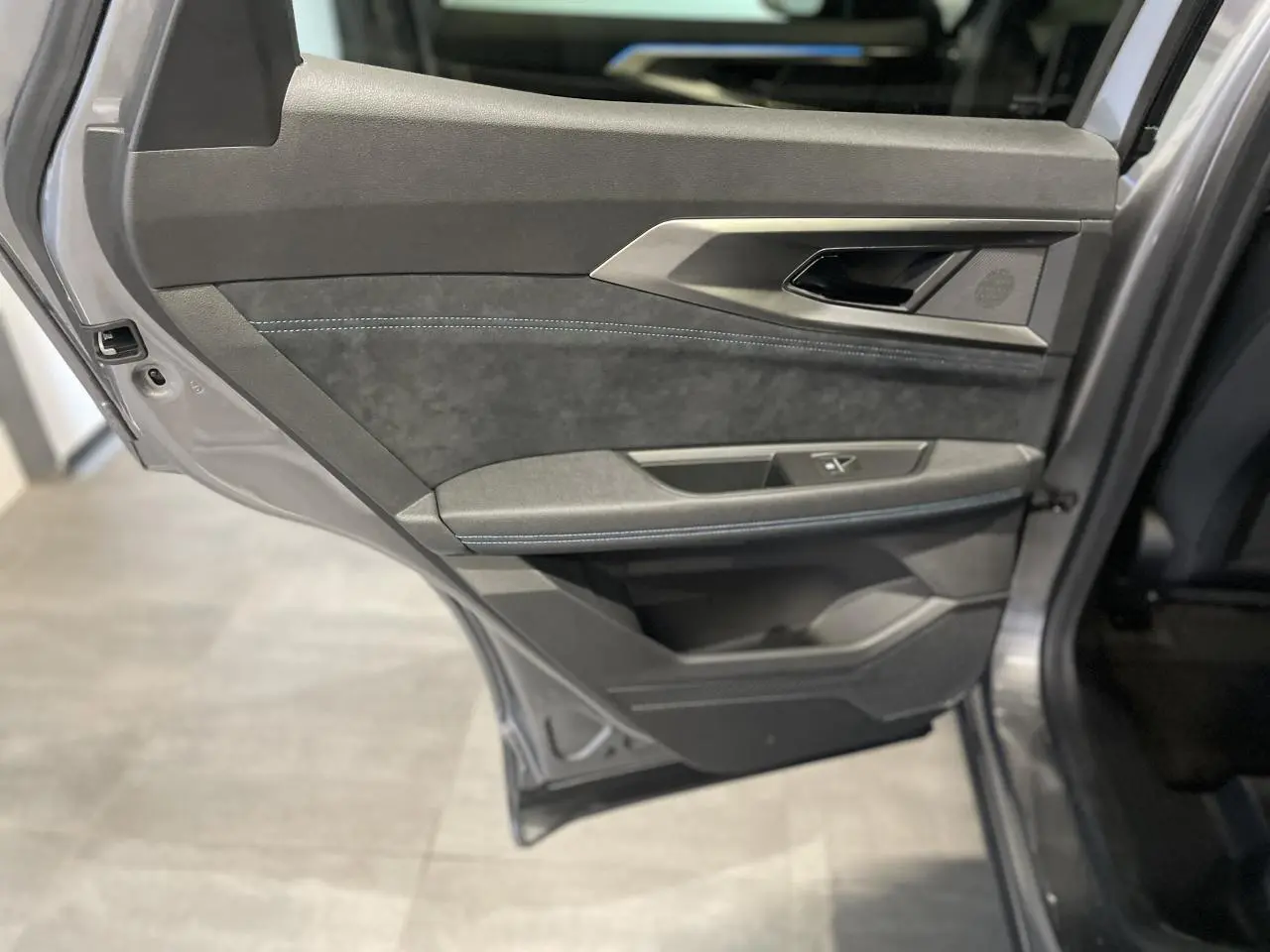 Gros plan sur la porte arrière gauche gris métallisé du Renault Austral avec garniture en Alcantara et surpiqûres bleues.