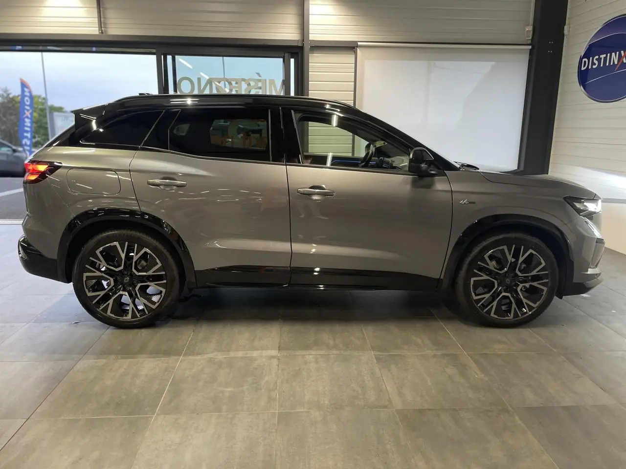 Profil droit d'un Renault Austral gris métallisé avec toit noir étoilé et jantes alliage noires en showroom.