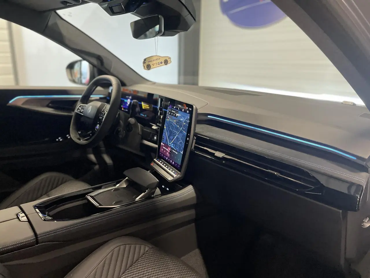 Intérieur Renault Austral 2025 vu côté conducteur, tableau de bord noir avec écran tactile vertical et éclairage bleu fin.