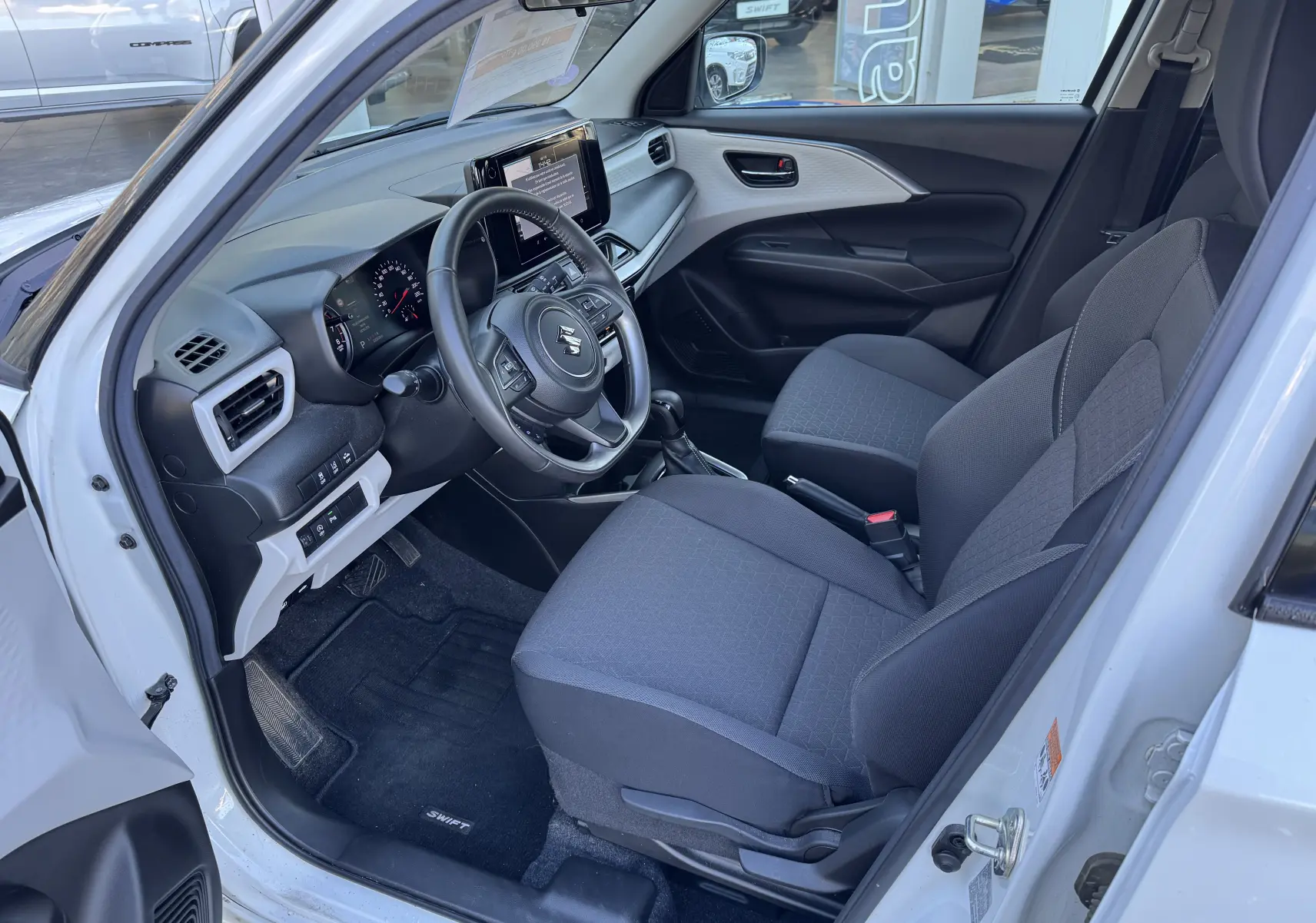 Vue intérieure côté conducteur de la Suzuki Swift 1.2 Dualjet Pack Auto Hybrid 2024, sièges gris et tableau de bord moderne.