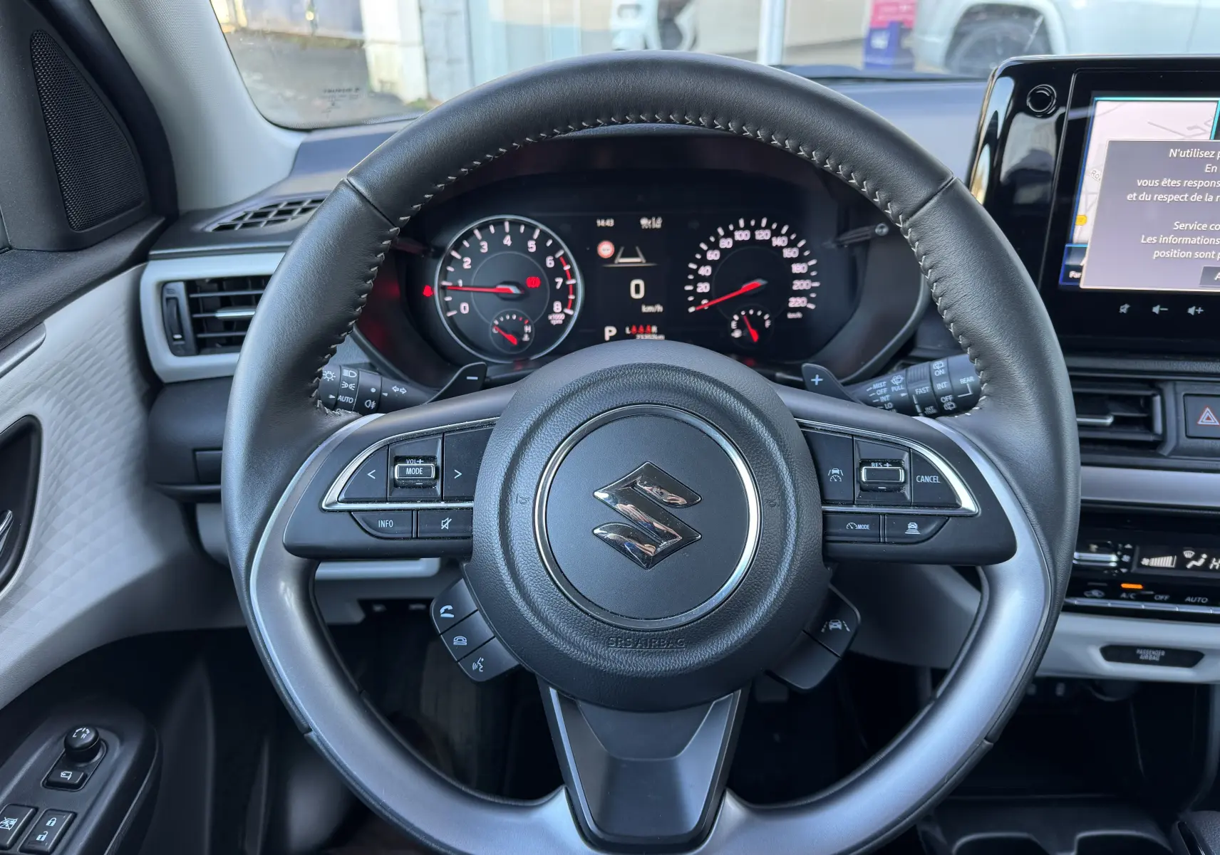 Vue intérieure centrée sur le volant noir et gris de la Suzuki Swift 2024 avec tableau de bord digital et écran tactile.