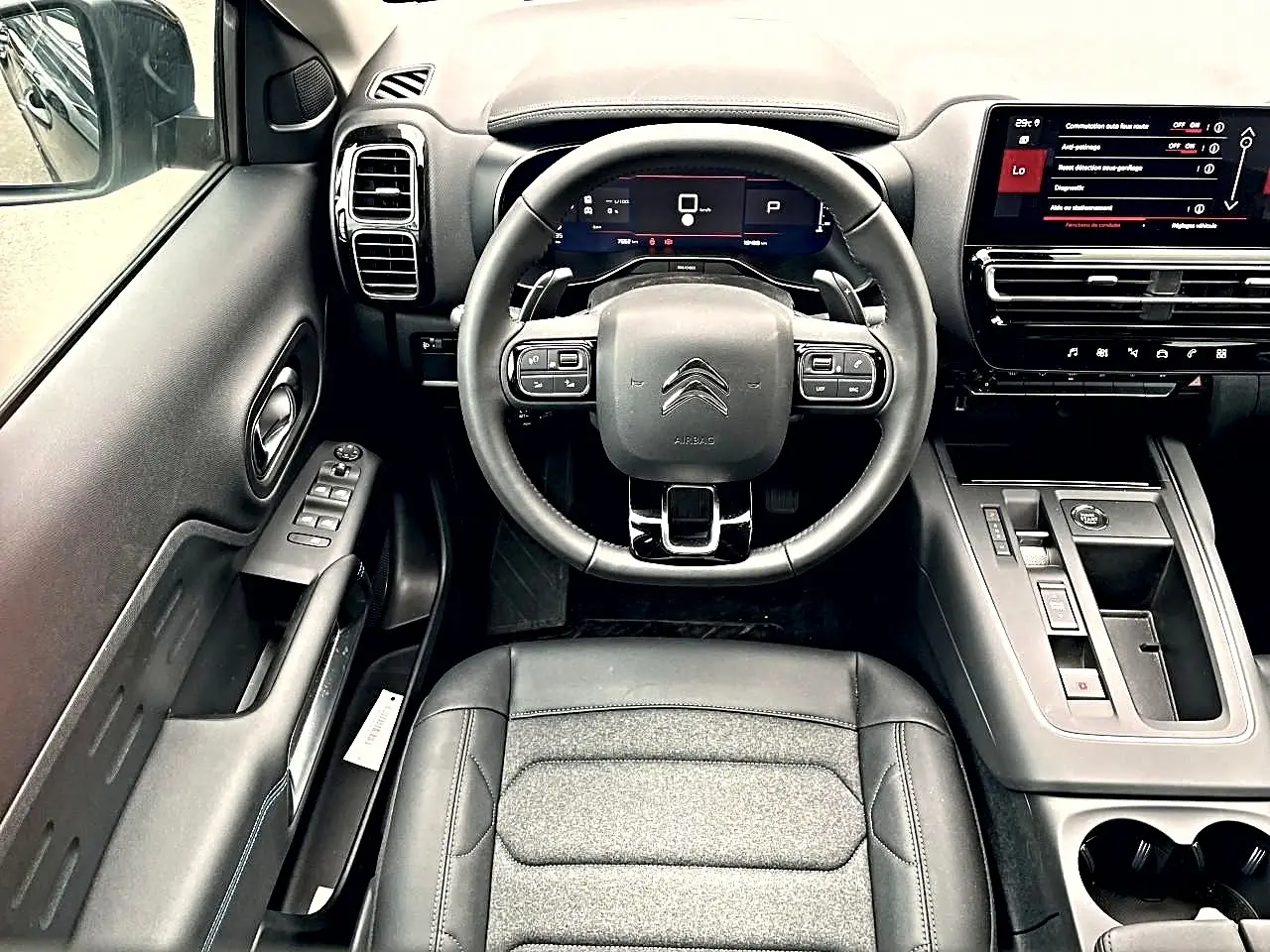 Vue intérieure centrée sur le volant et tableau de bord noir du Citroën C5 Aircross hybride 2025 avec écran tactile et commandes intégrées.