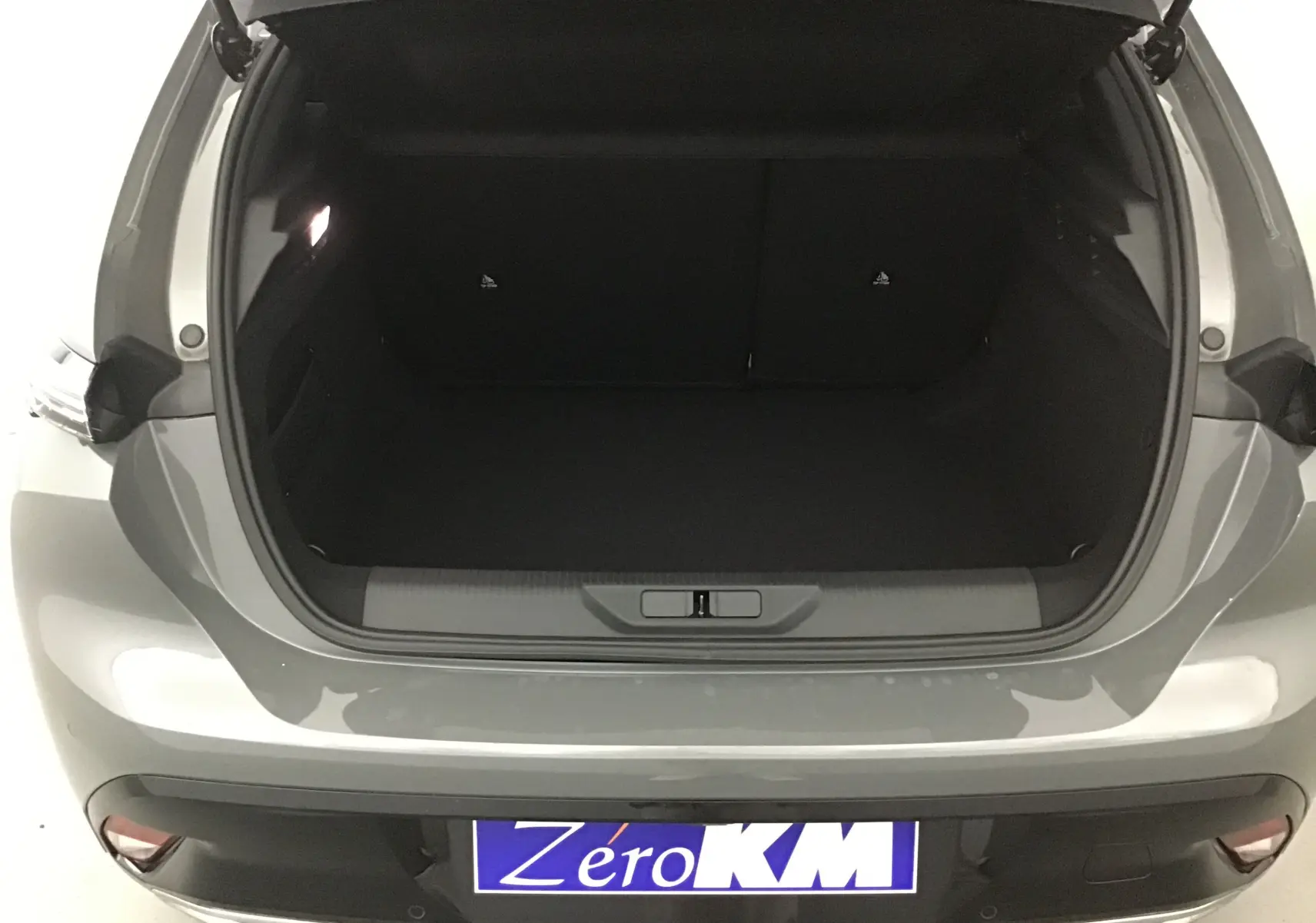 Coffre ouvert vu de l'arrière d'une Peugeot 308 gris selenium, montrant l'espace de chargement vide et propre.