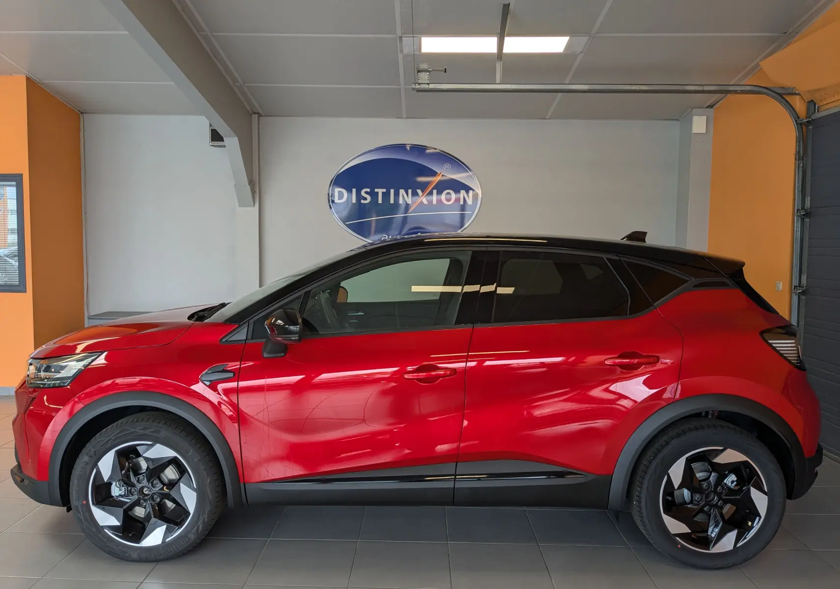 Profil côté gauche du Renault Captur 2025 rouge flamme avec toit noir et jantes alliage 18 pouces en intérieur showroom.