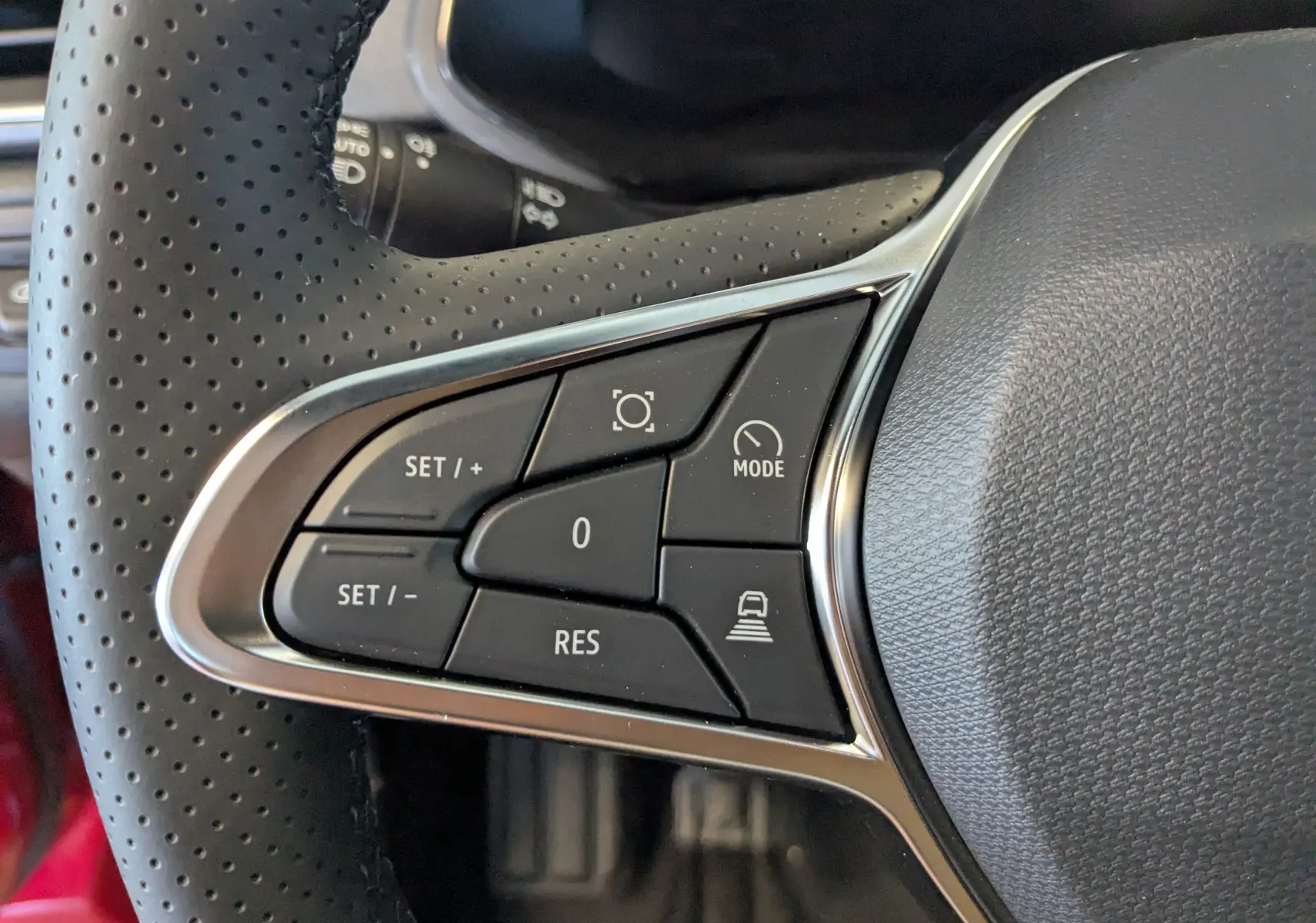 Gros plan sur les commandes du volant en cuir perforé du Renault Captur E-Tech 2025, boutons de régulateur adaptatif visibles.