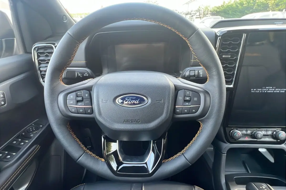 Volant cuir noir avec surpiqûres marron et commandes multifonctions du Ford Ranger 2025, tableau de bord et écran tactile visibles.