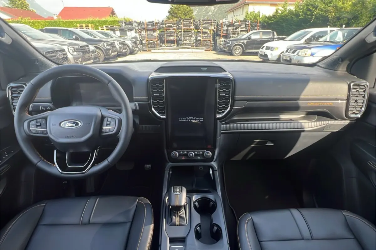 Intérieur du Ford Ranger Wildtrak 2025 vu de face, tableau de bord noir avec coutures orange et écran central vertical.