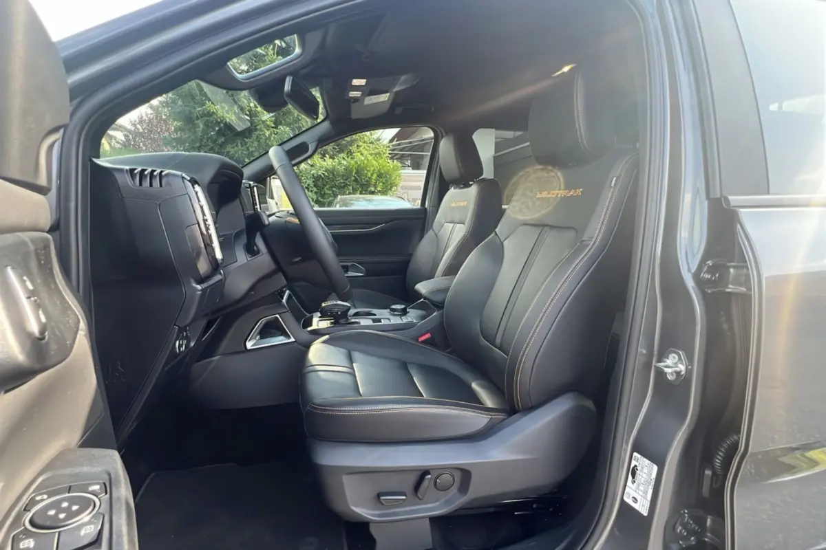 Intérieur côté conducteur du Ford Ranger Wildtrak gris carbone, sièges cuir noirs avec surpiqûres orange et logo Wildtrak.