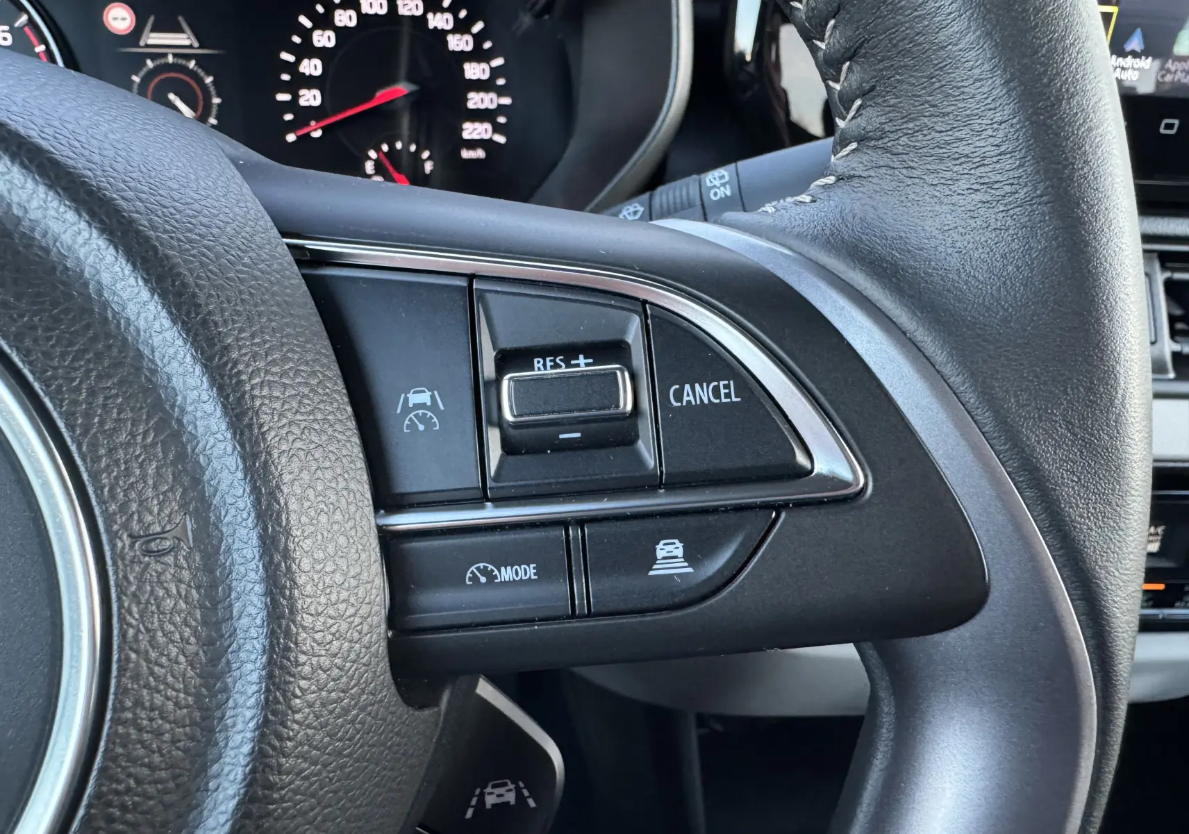 Gros plan sur les commandes de régulateur de vitesse au volant cuir noir de la Suzuki Swift blanche 2025 hybride.